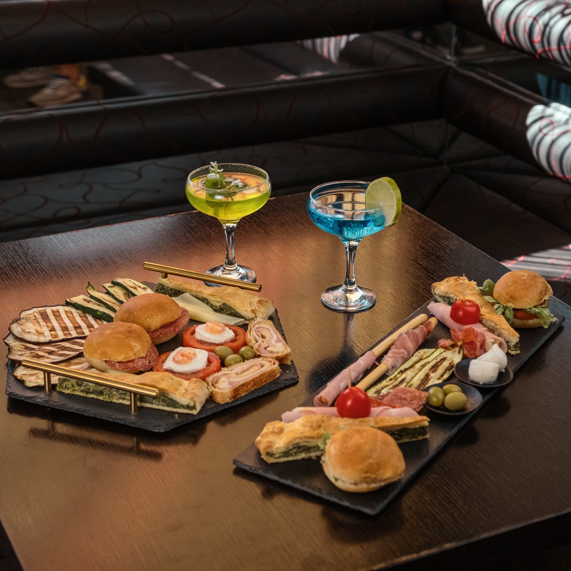 Due vassoi di cibo e due cocktail su un tavolo di legno scuro.