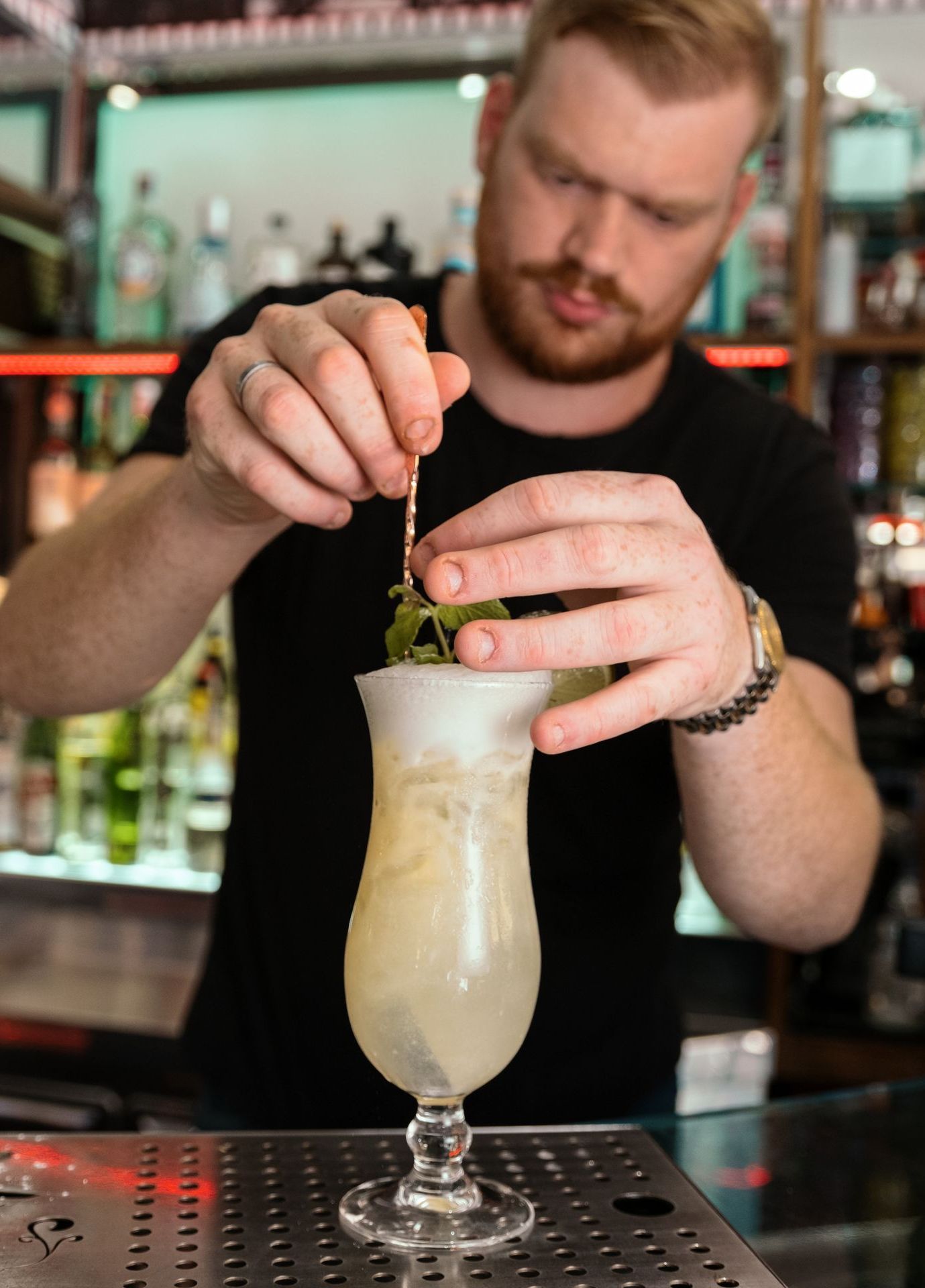 Barista che guarnisce un cocktail con un rametto di menta in un bar.