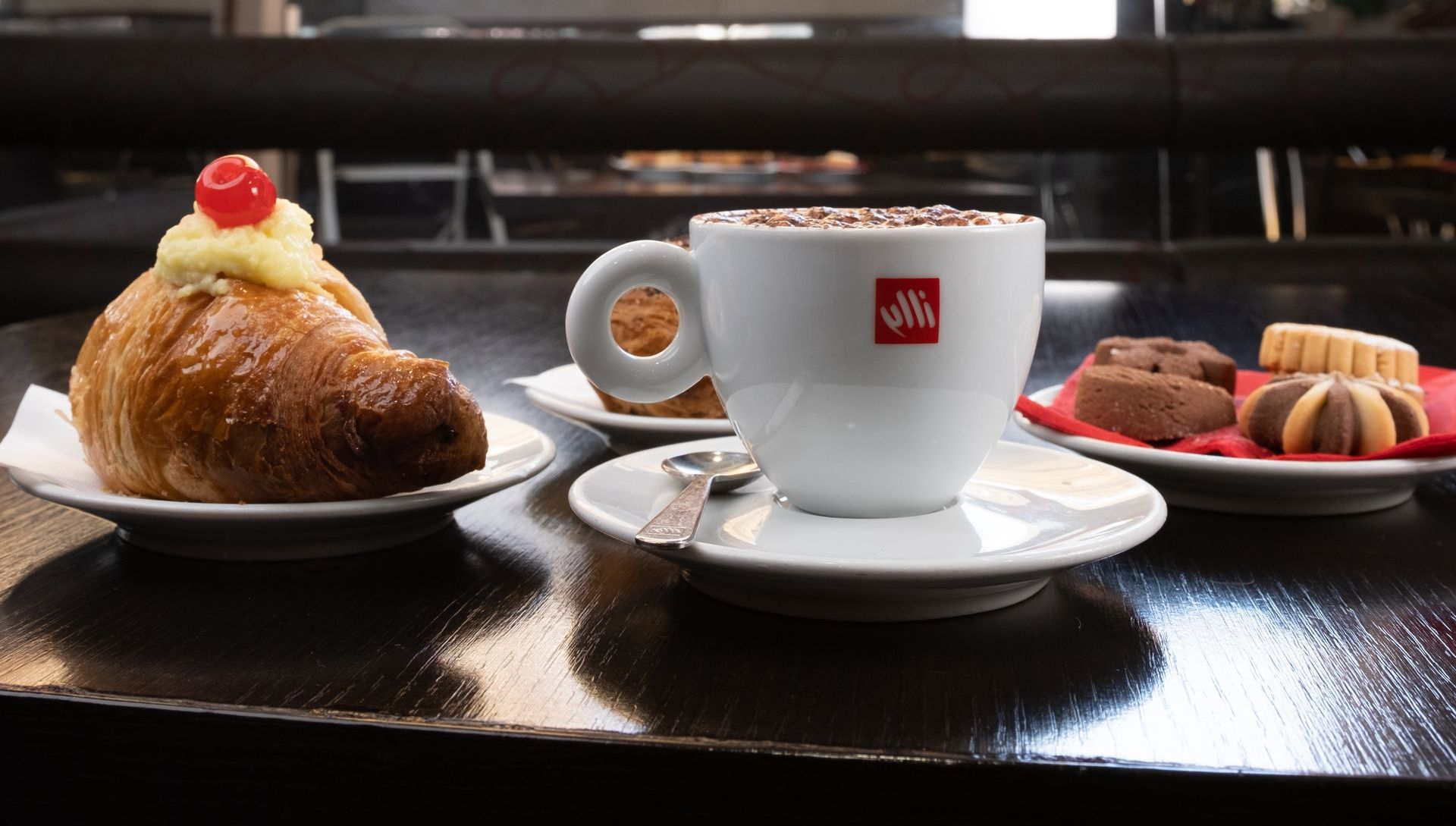 Tazzina da caffè con pasticcini e biscotti su un tavolo scuro, ambiente da bar.