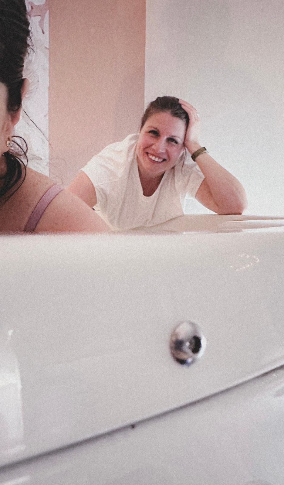 Persona sonriente apoyada en el borde de una bañera blanca en un baño.