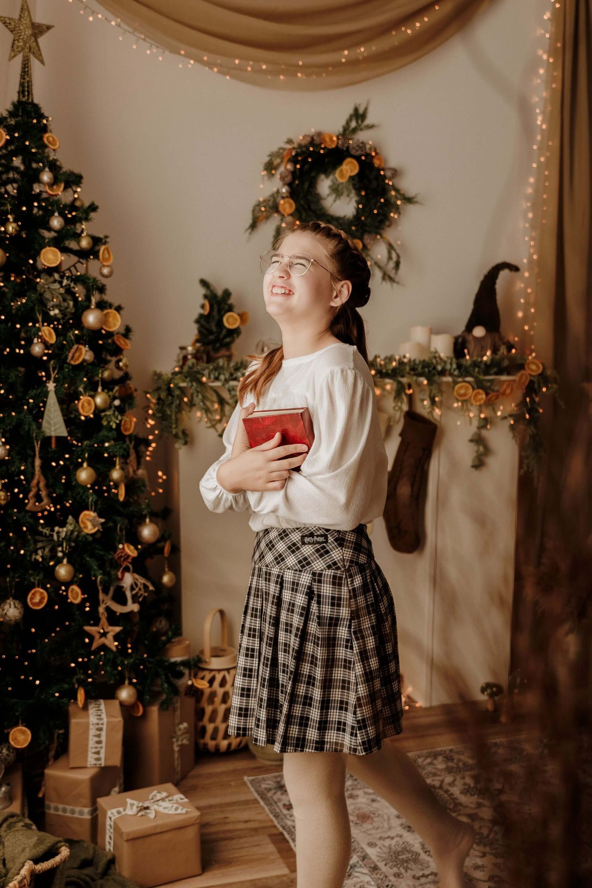 Persona sosteniendo un regalo rojo en una habitación decorada junto a un árbol de Navidad y una corona.