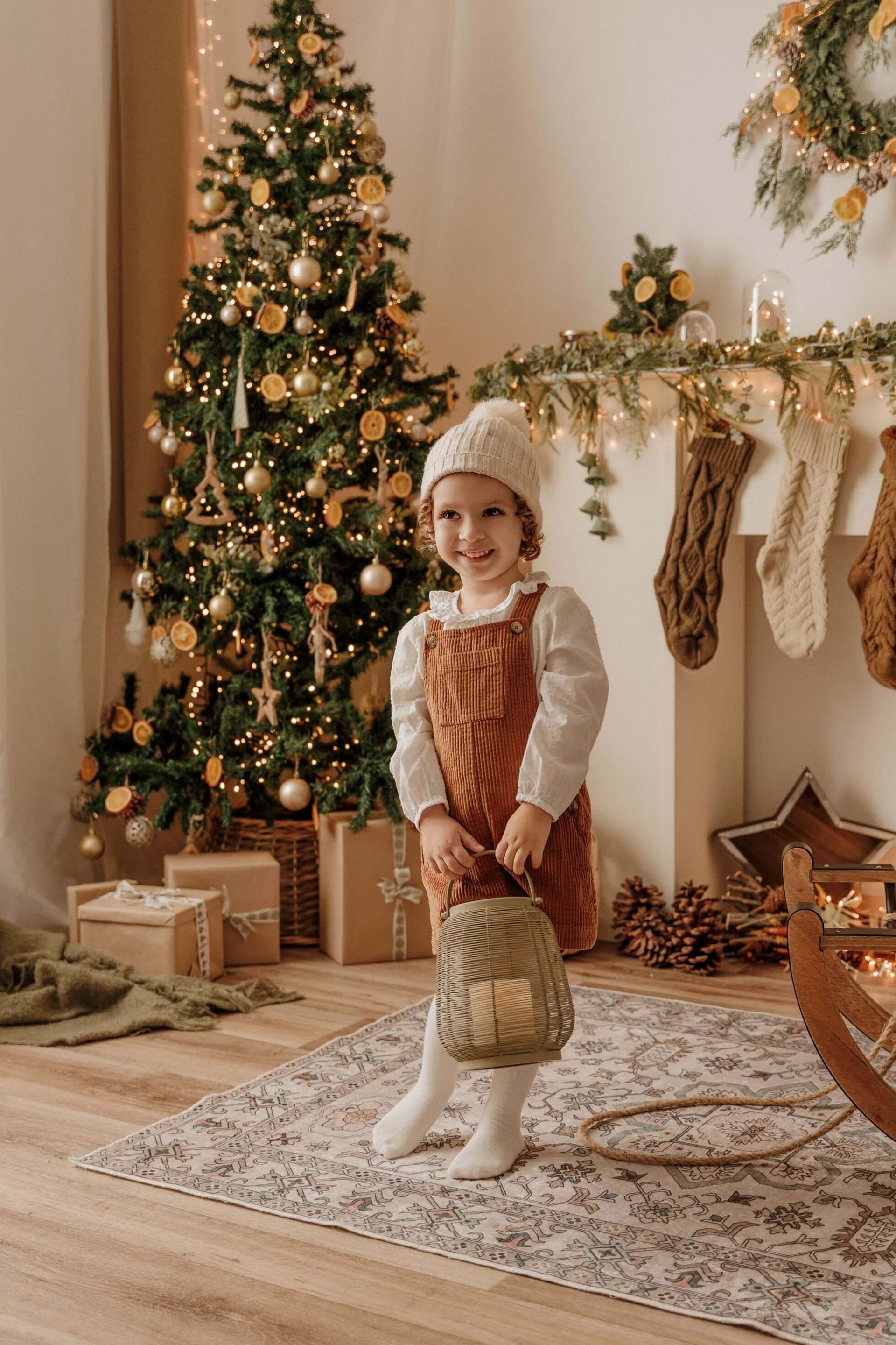 Un niño con gorro de Papá Noel de pie junto a un árbol de Navidad decorado en una acogedora sala de estar.
