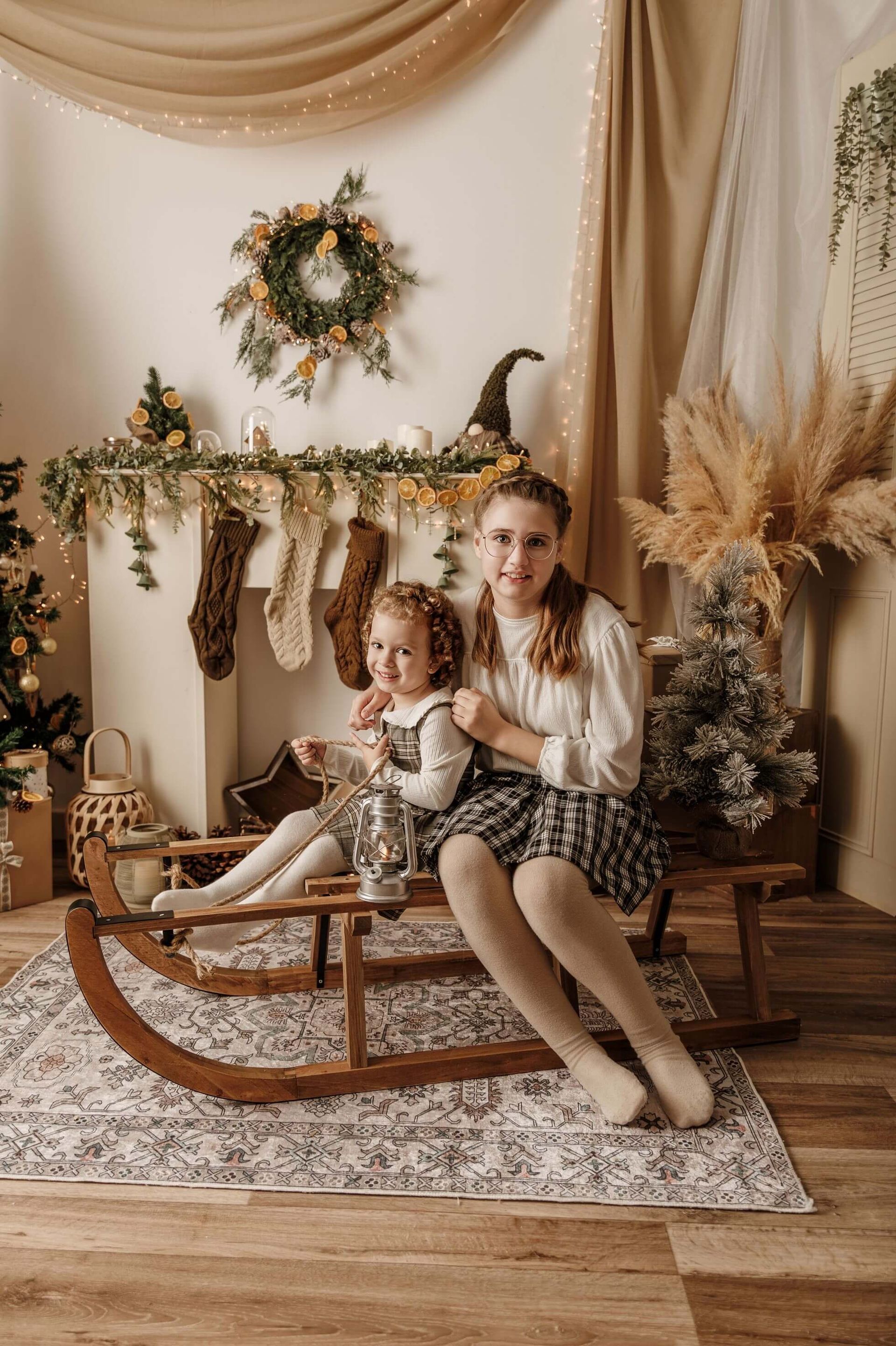 Dos niños sentados en un caballito mecedor de madera en una acogedora habitación de color beige decorada para las fiestas.