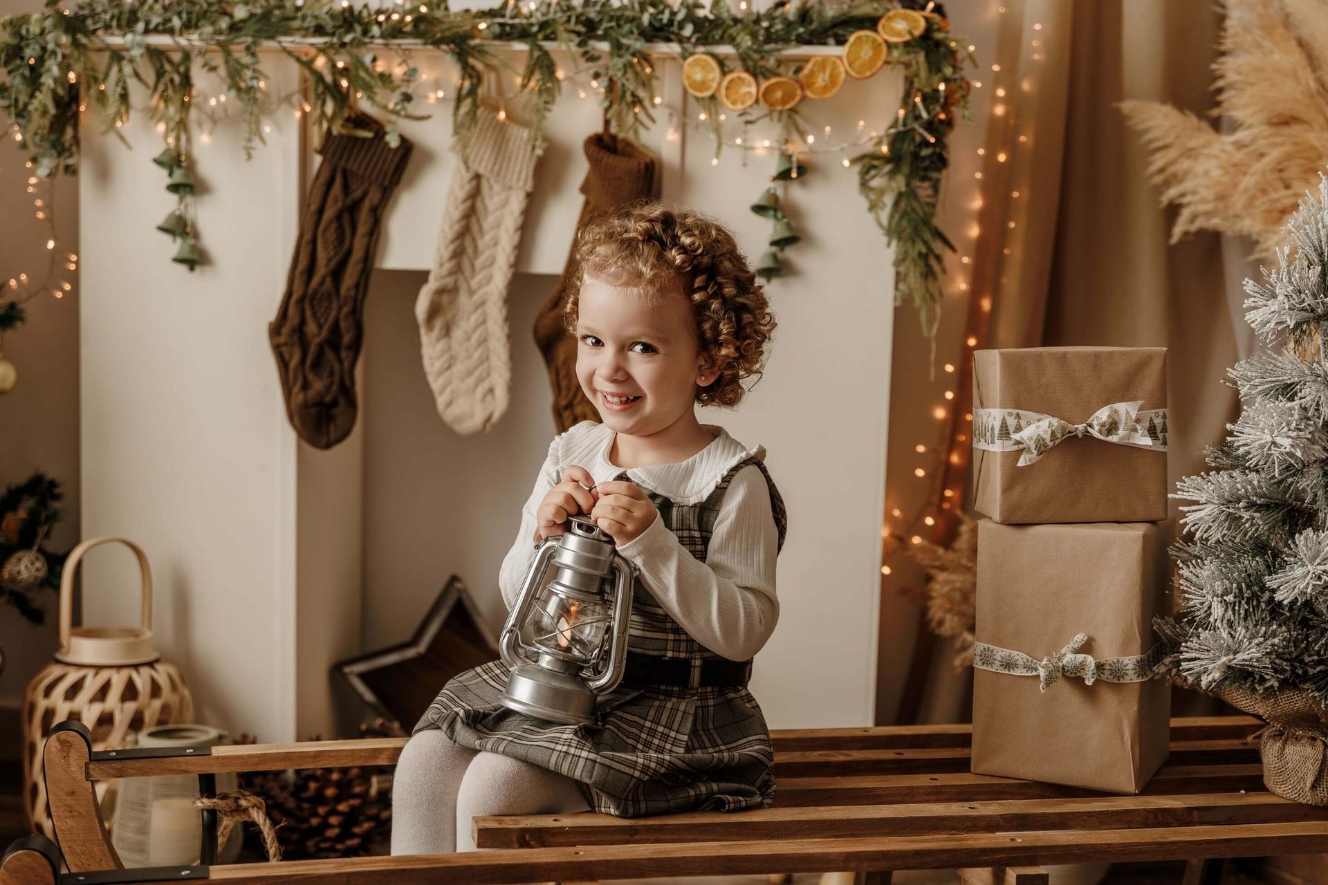 Un niño sostiene una linterna en un acogedor ambiente navideño con calcetines, guirnaldas y regalos envueltos.