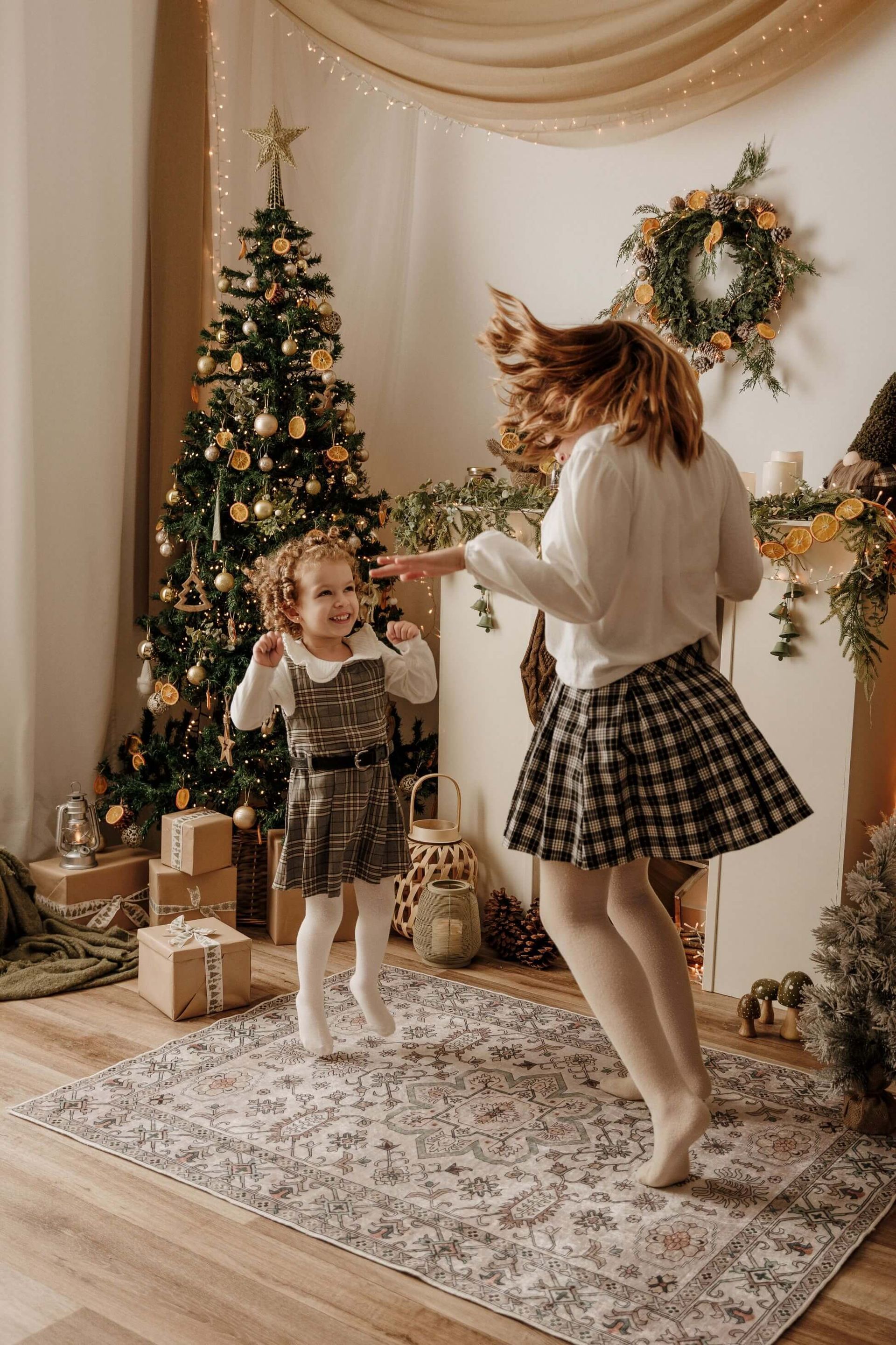 Mujer y niño bailando en una habitación decorada para Navidad con árbol, corona y regalos envueltos.