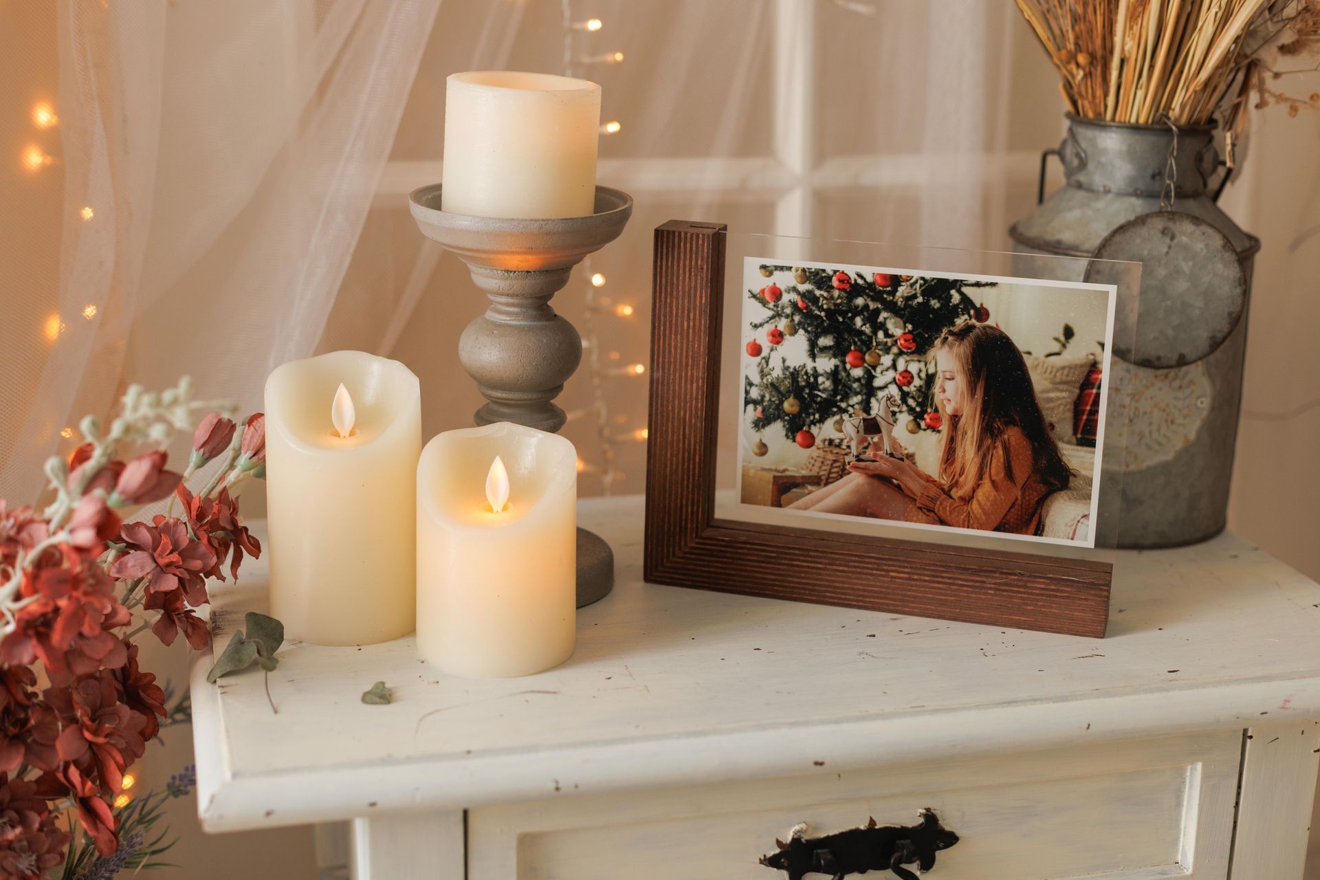 Cómoda iluminada con velas, con una foto enmarcada, flores y un jarrón rústico en una habitación acogedora.