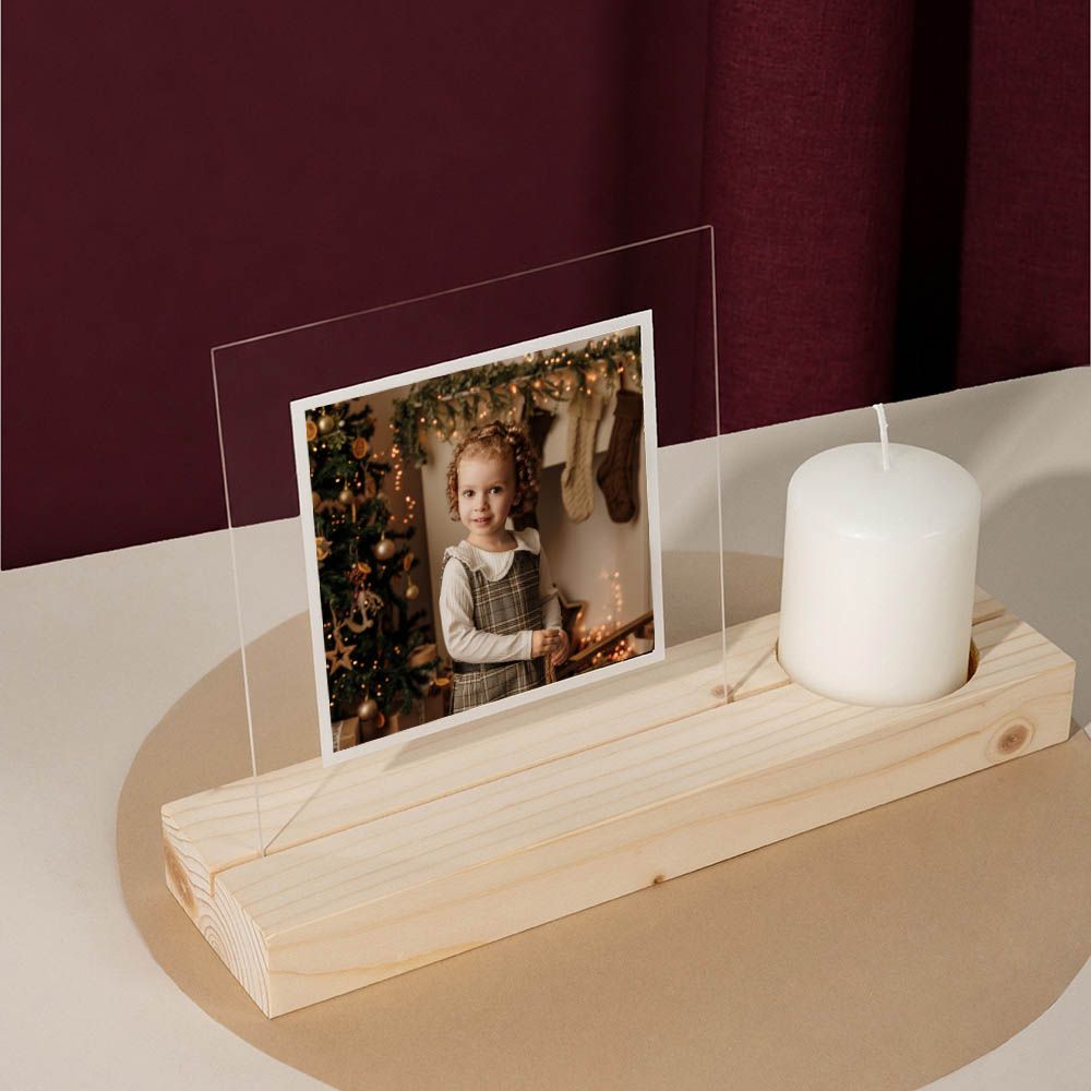 Portavelas decorativo de madera con un pequeño retrato enmarcado y una vela blanca sobre una superficie beige.