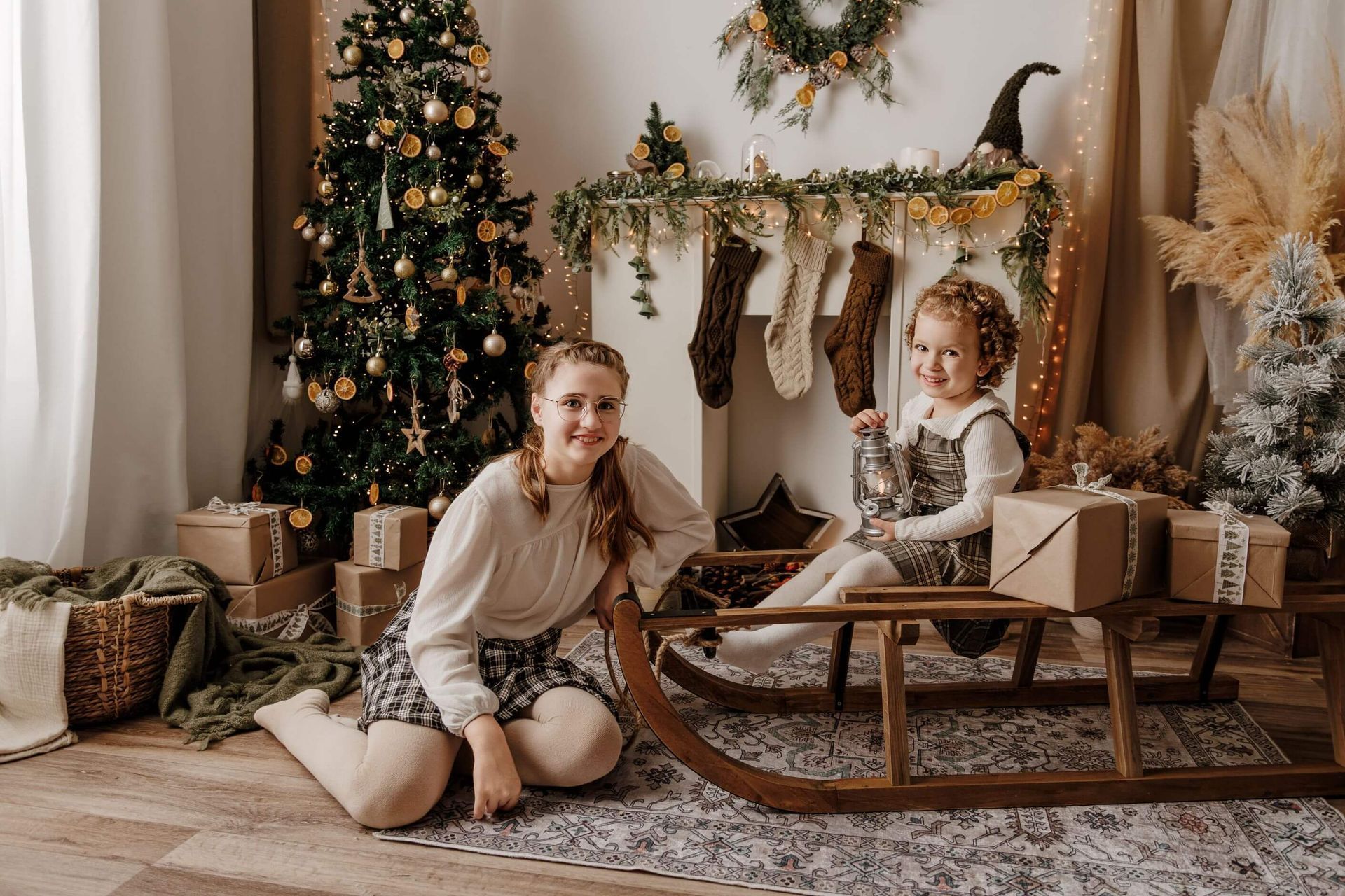 Dos niñas junto a un árbol de Navidad y una chimenea, rodeados de regalos envueltos en una acogedora
