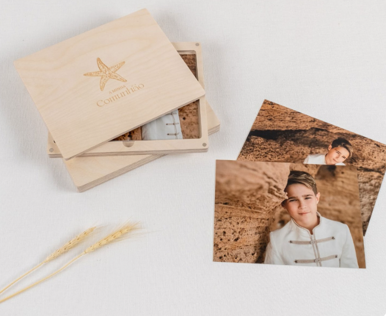 Tarjetas fotográficas impresas y una caja de papelería color canela sobre una superficie blanca, con dos bolígrafos dorados cerca.