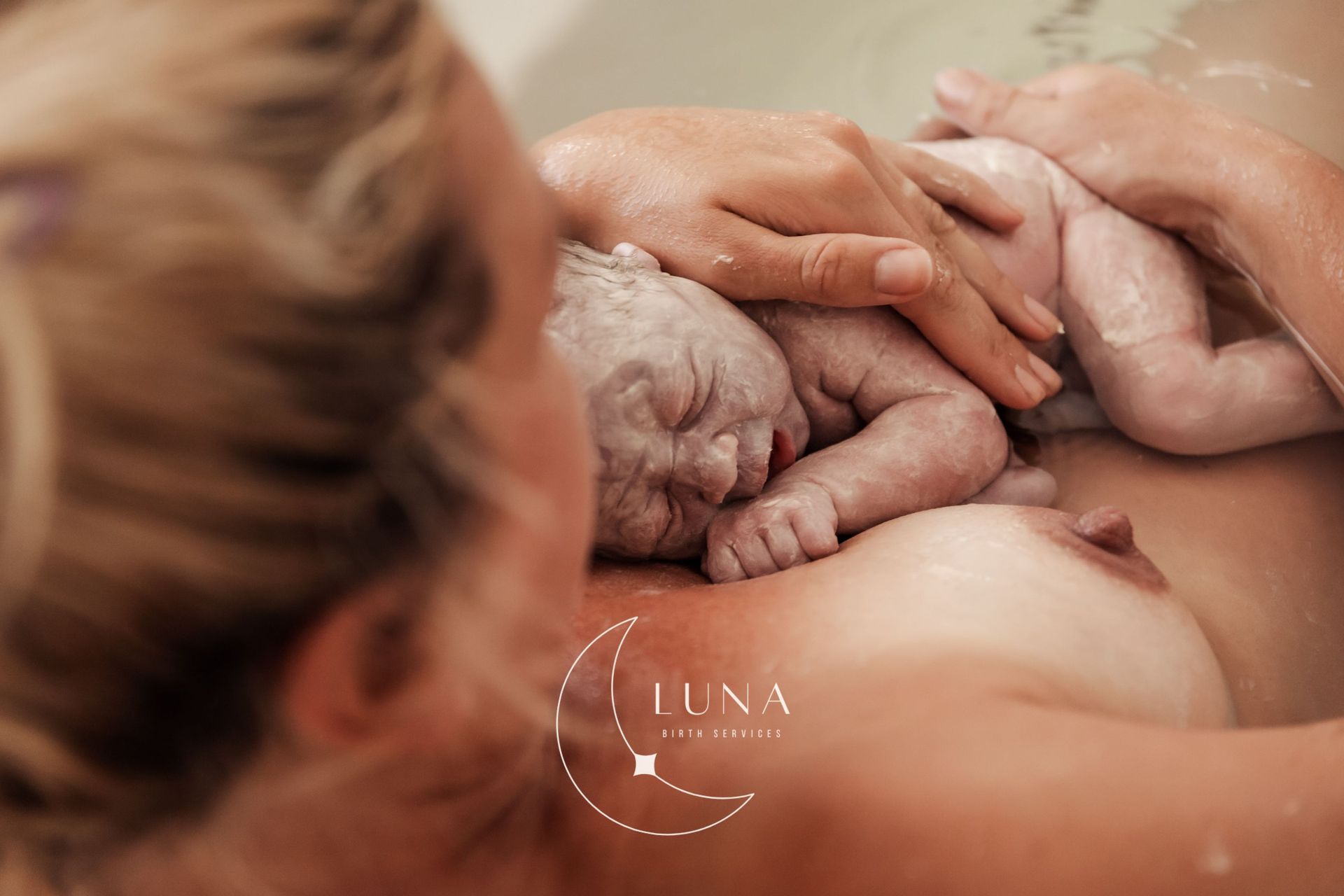 Unas manos sostienen con delicadeza a un bebé recién nacido sobre el pecho de uno de sus padres, bajo una luz cálida y suave.
