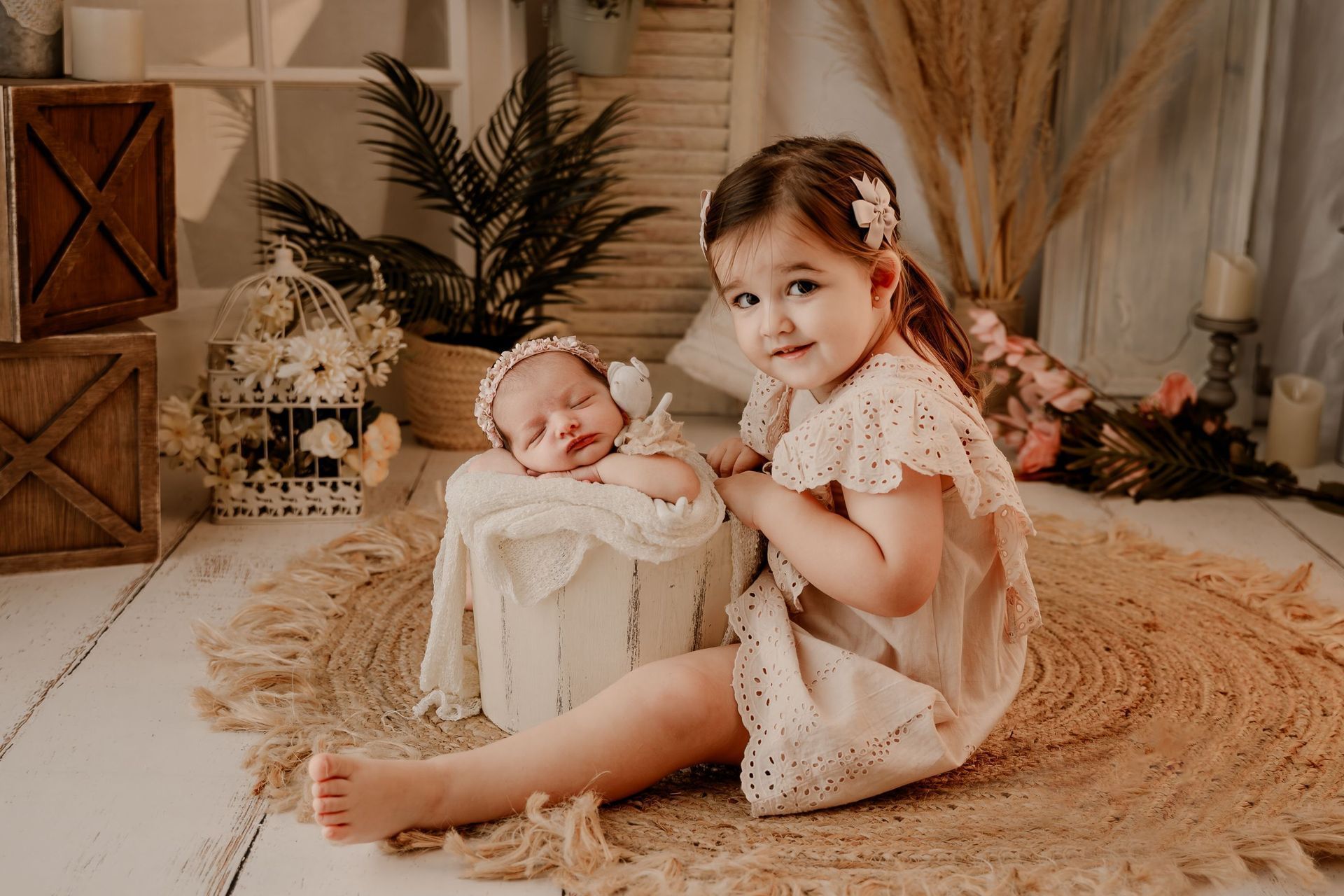 Dos niños sentados sobre una alfombra beige en una acogedora habitación con flores secas y una decoración cálida.