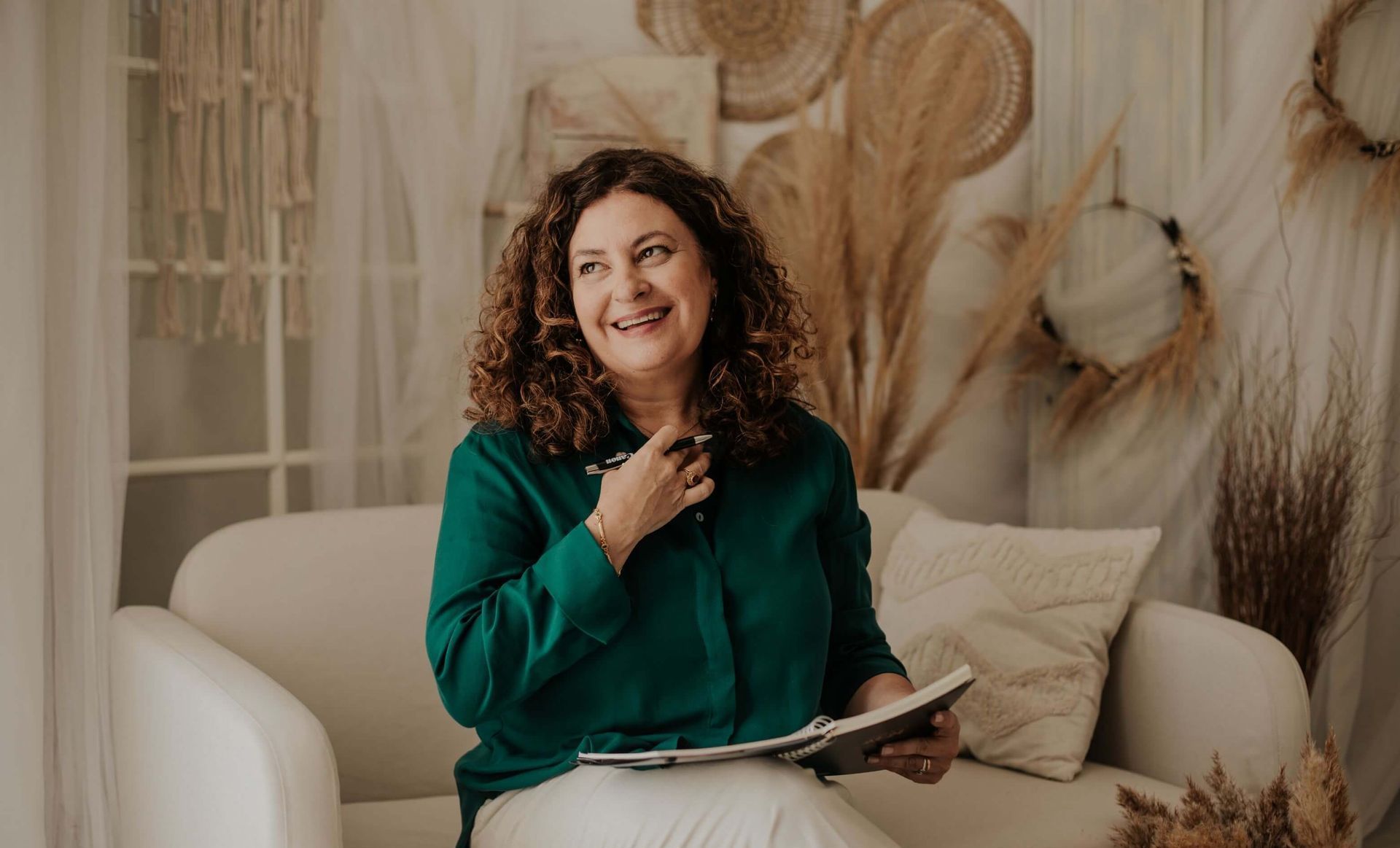 Una mujer está sentada en un sofá sosteniendo un libro y sonriendo.