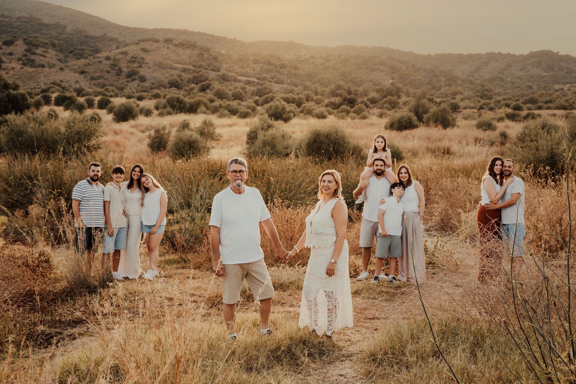 Grupo de personas de pie en un campo seco cubierto de hierba con colinas al fondo, al atardecer.