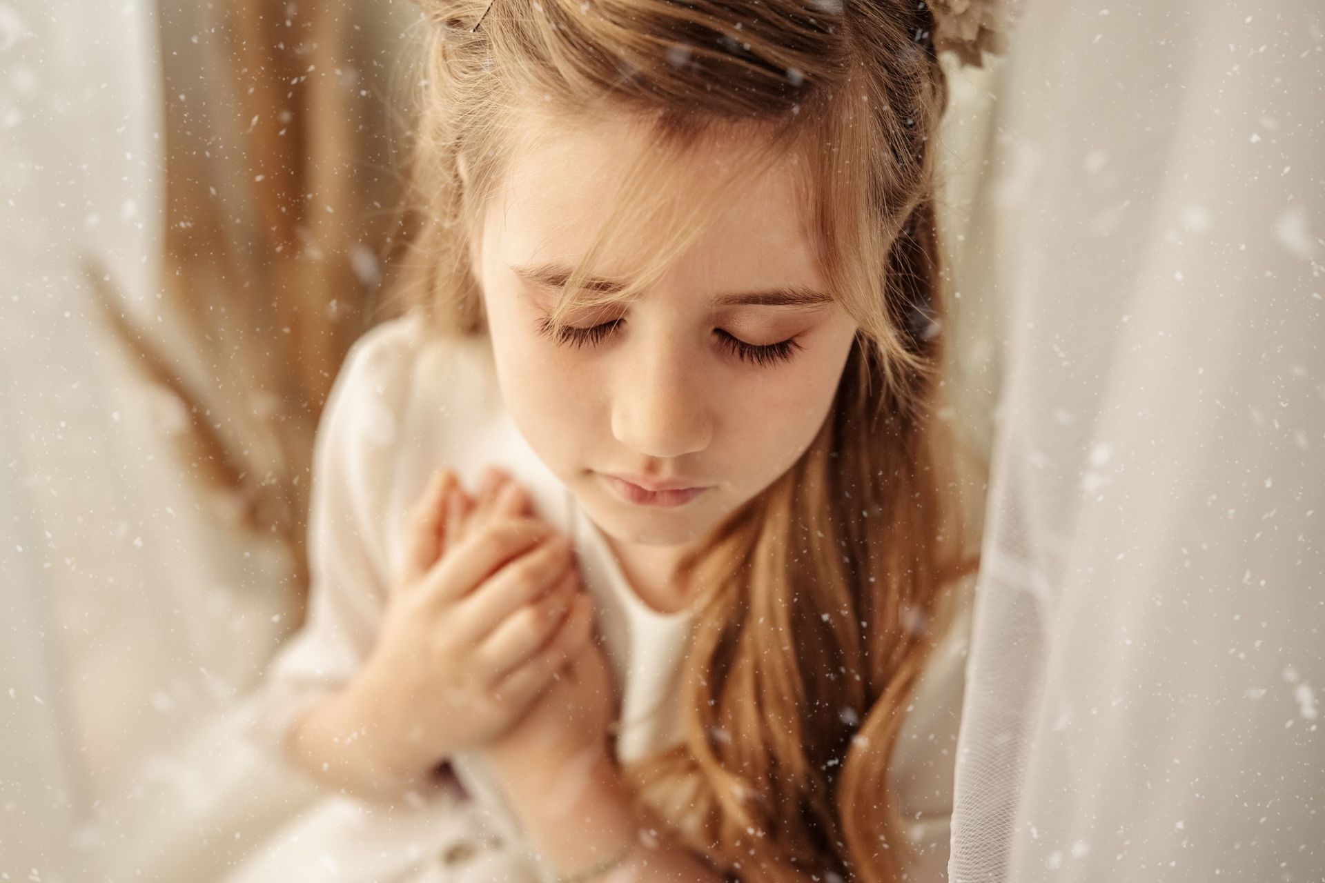 Niña con los ojos cerrados sosteniendo un peluche blanco, bajo una luz cálida y suave con copos que caen como nieve.
