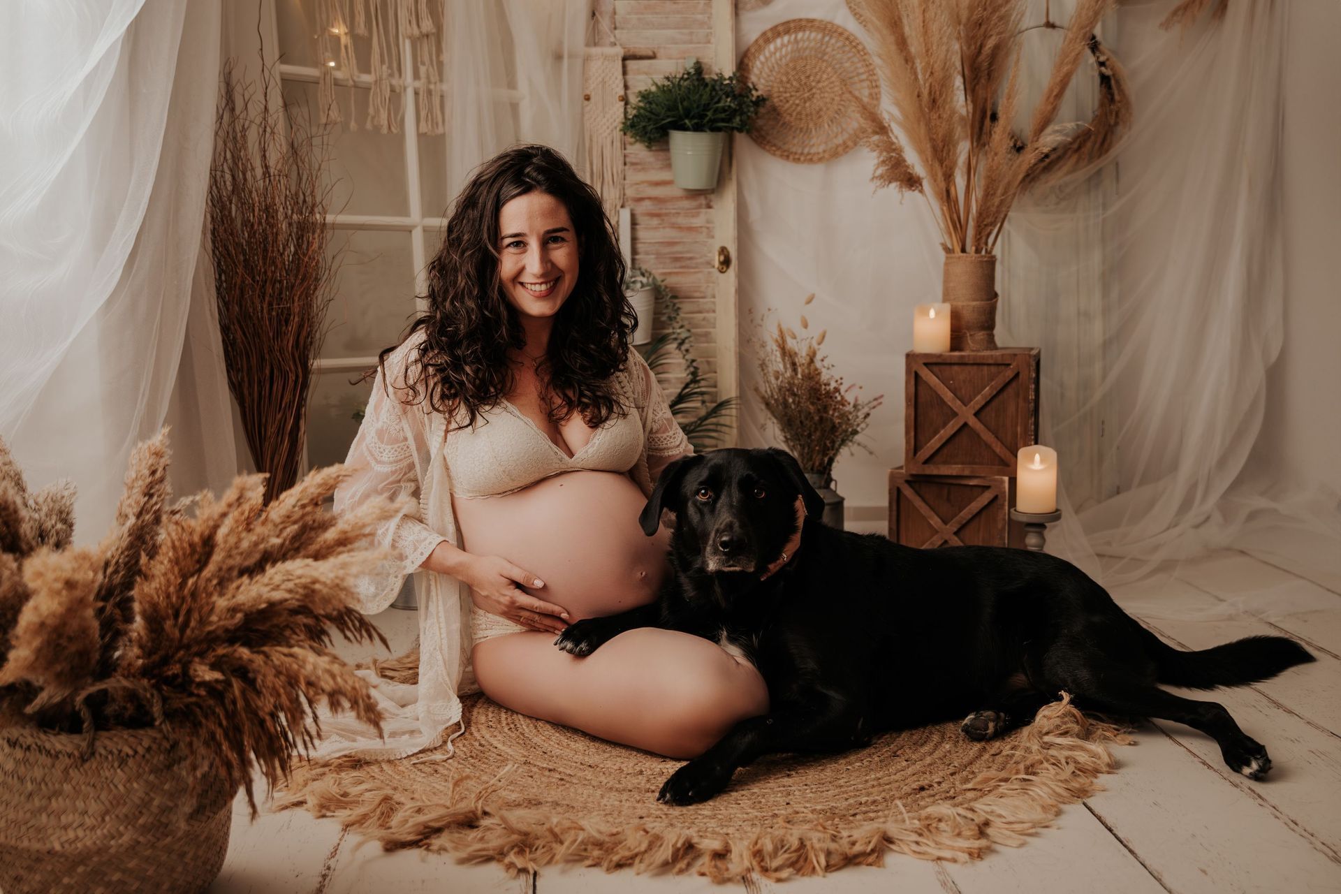Mujer embarazada sentada con su perro negro en un estudio de estilo bohemio en tonos beige suaves.