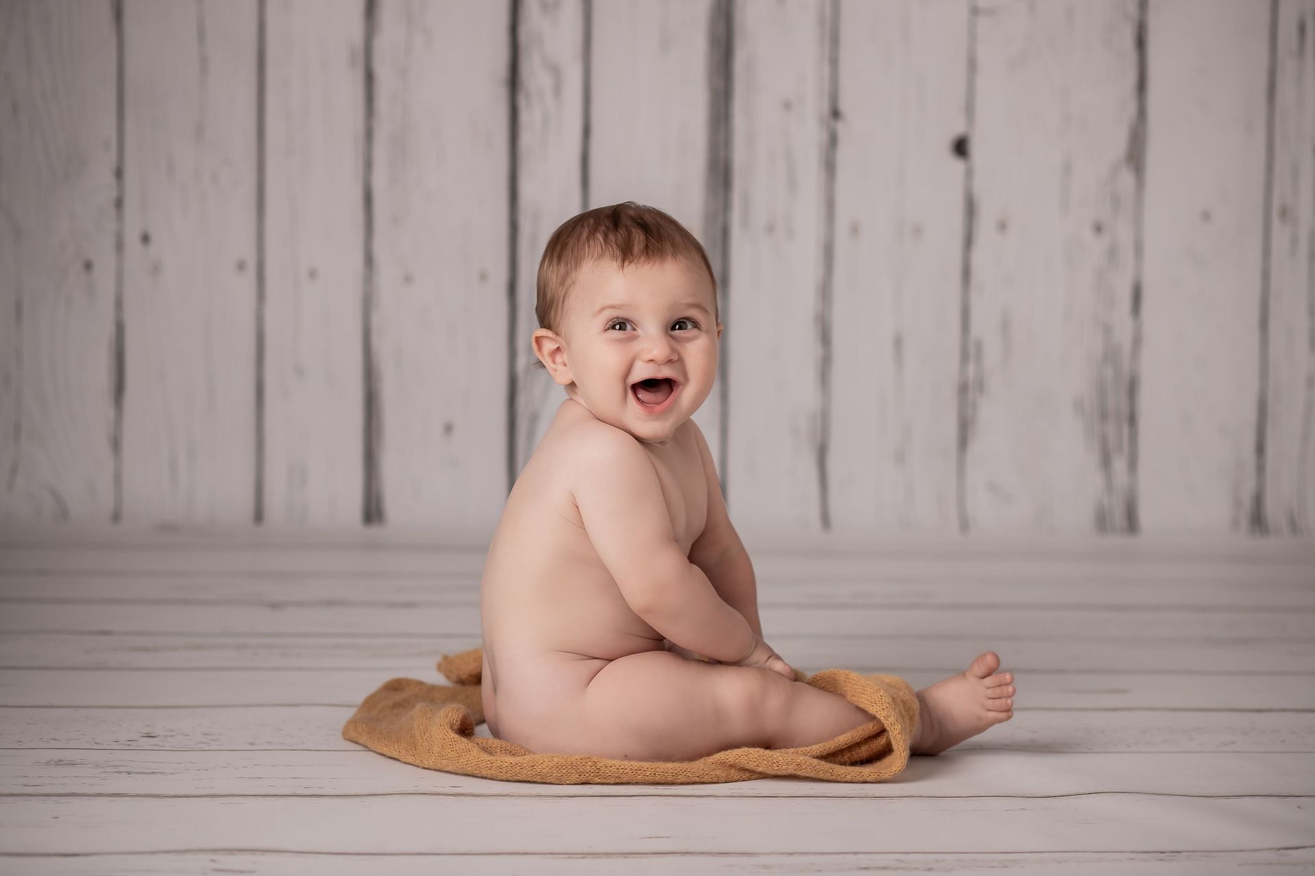 Un bebé sonriente está sentado sobre una pequeña estera tejida, con un fondo de madera clara.