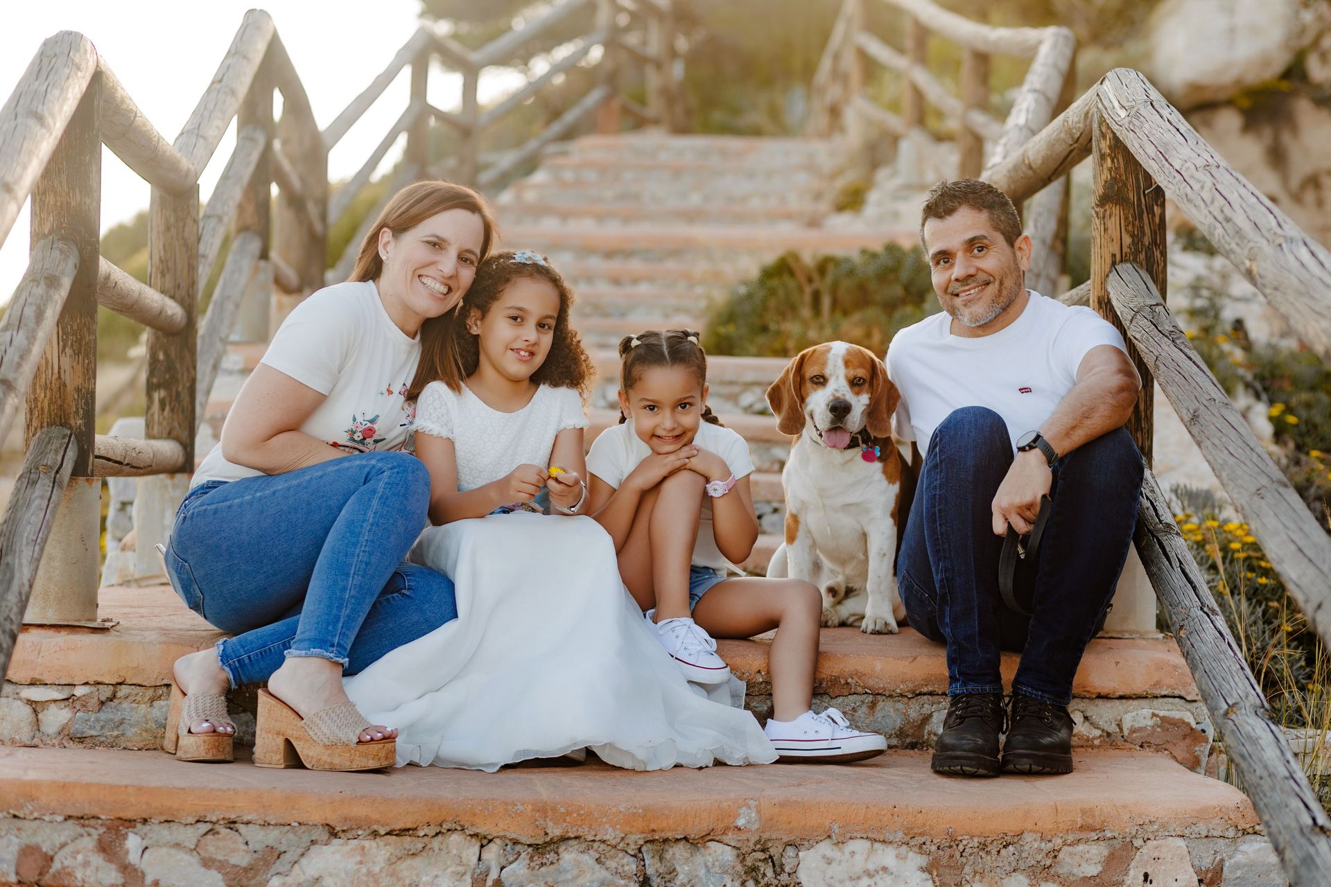 Una familia sentada en unos escalones de piedra al aire libre con un perro pequeño, sonriendo a la cámara.