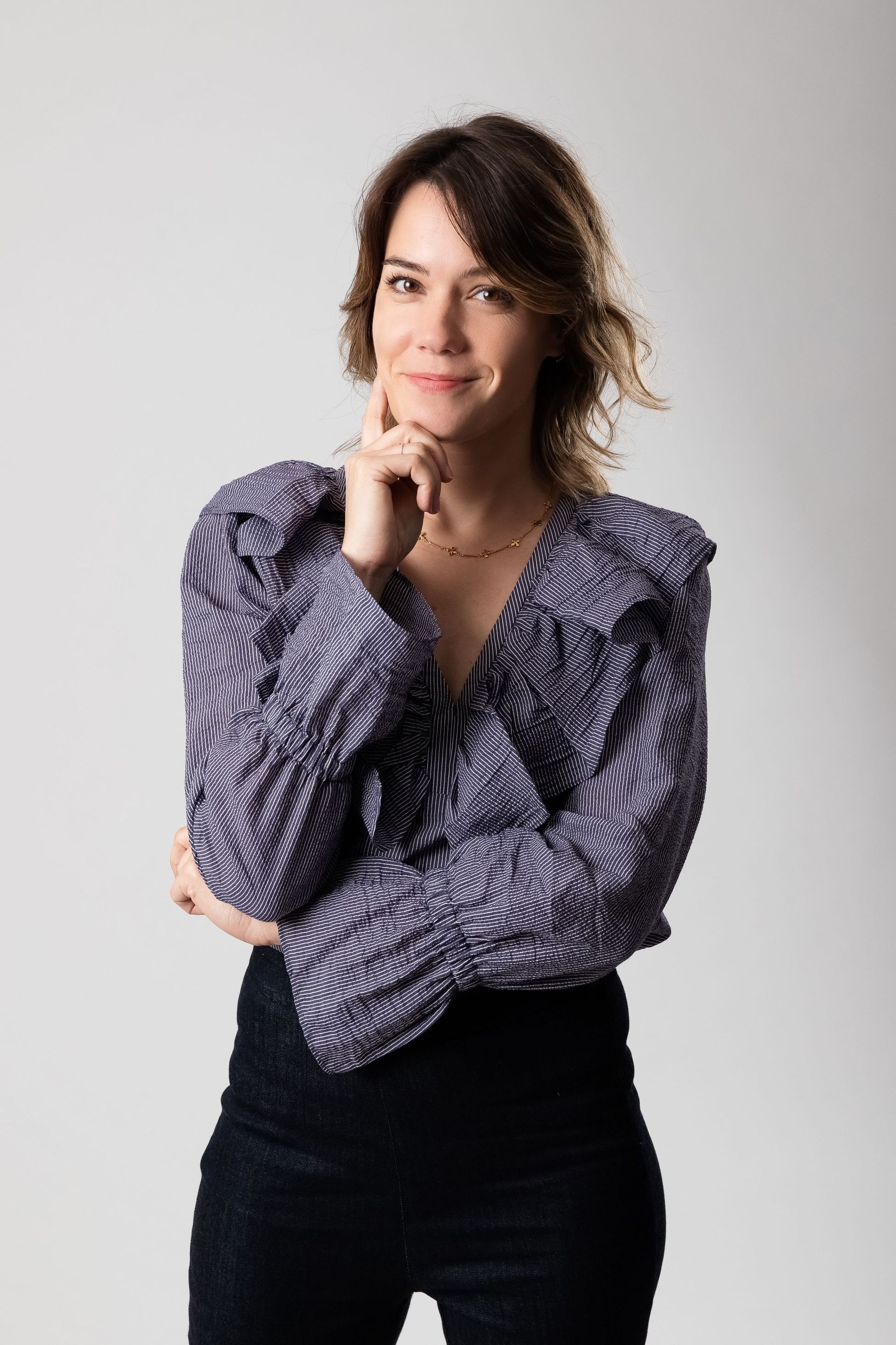 Persona de pie con la mano en la barbilla, vestida con una blusa estampada y una falda negra sobre un fondo claro.