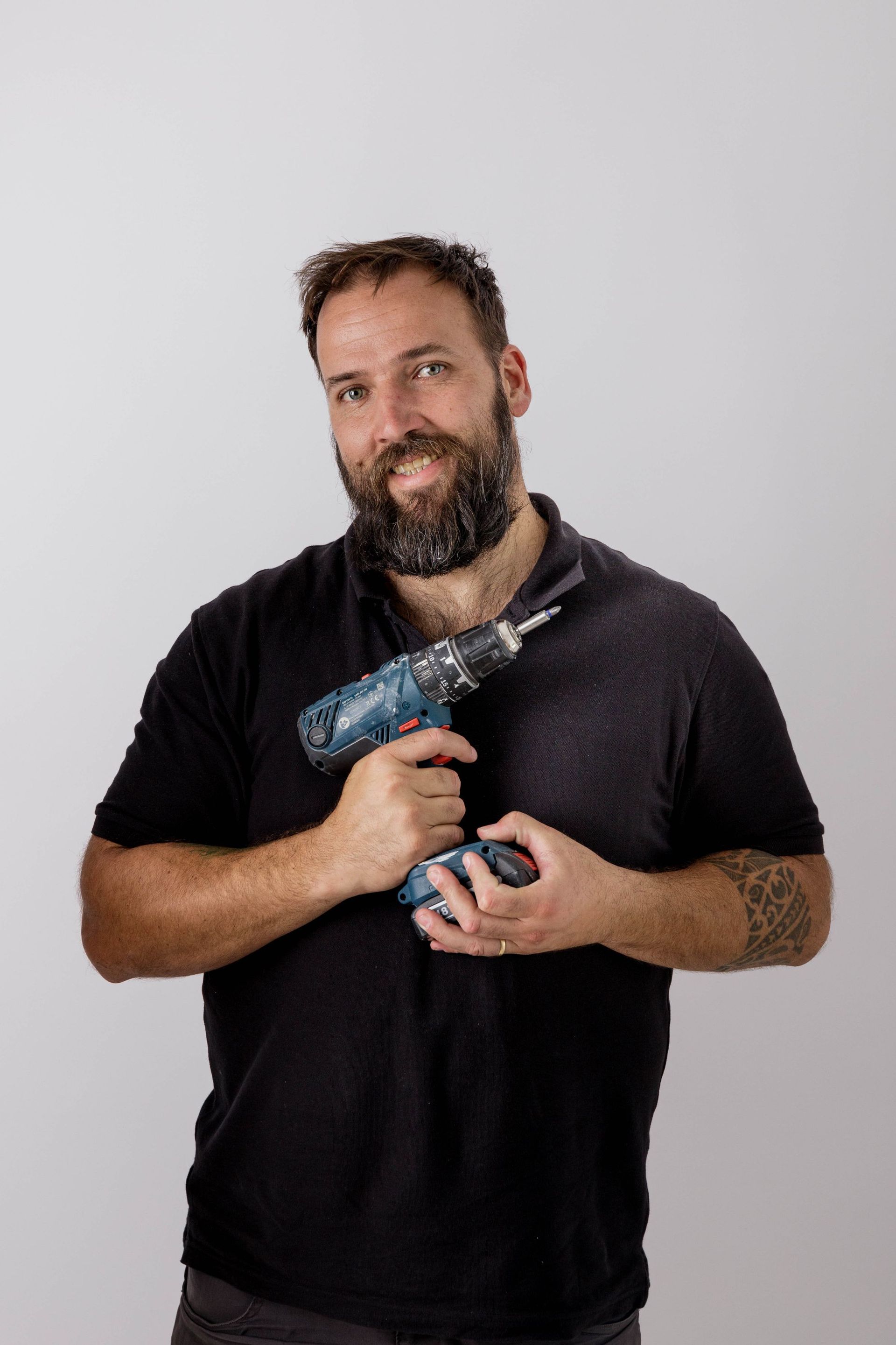 Hombre con un taladro azul, vestido con una camisa negra, sobre un fondo gris claro.