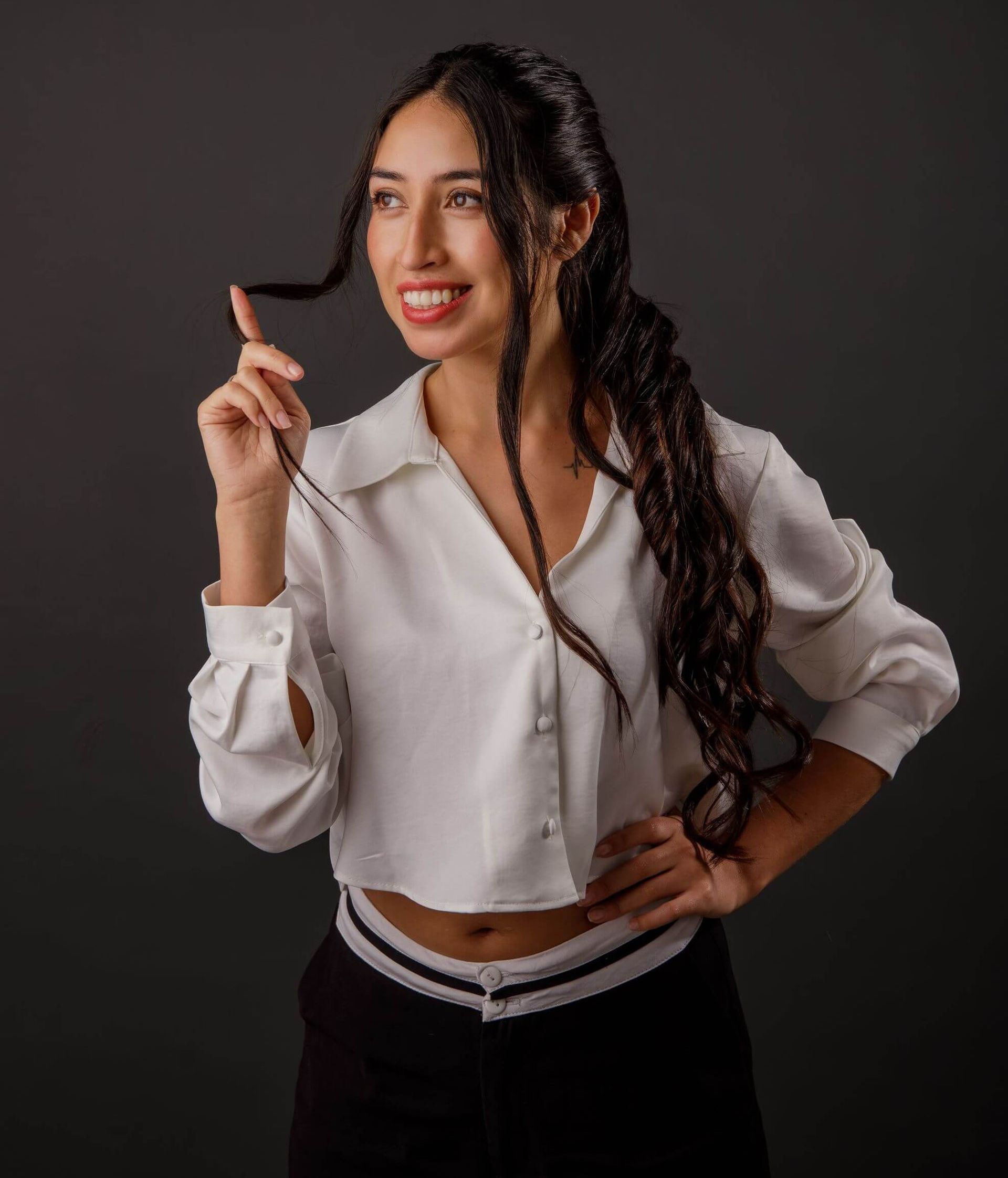 Mujer con camisa blanca sonriendo y sosteniendo un lápiz contra un fondo oscuro de estudio.