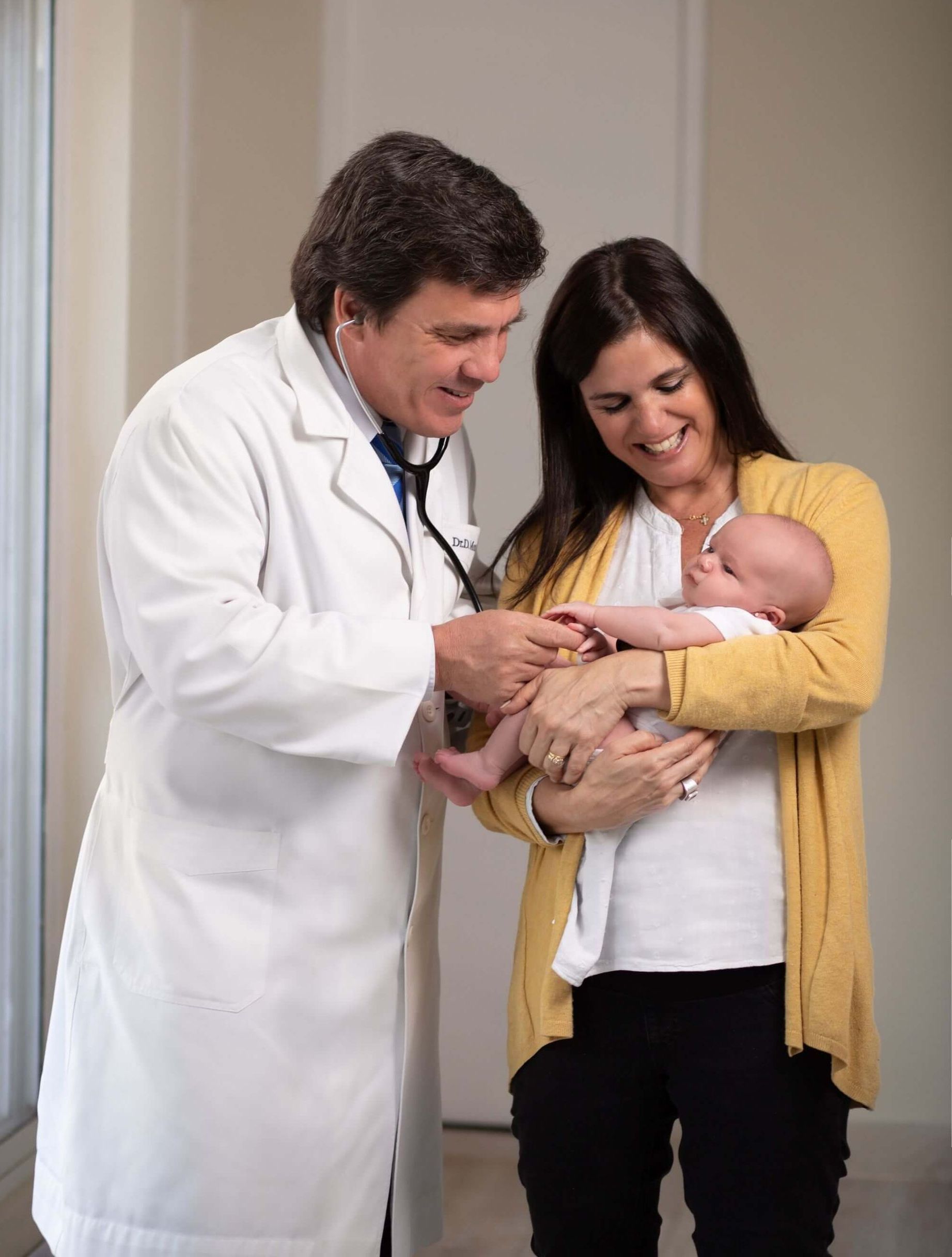 Un médico examina a un recién nacido mientras uno de los padres, sonriendo, sostiene al bebé en una clínica.