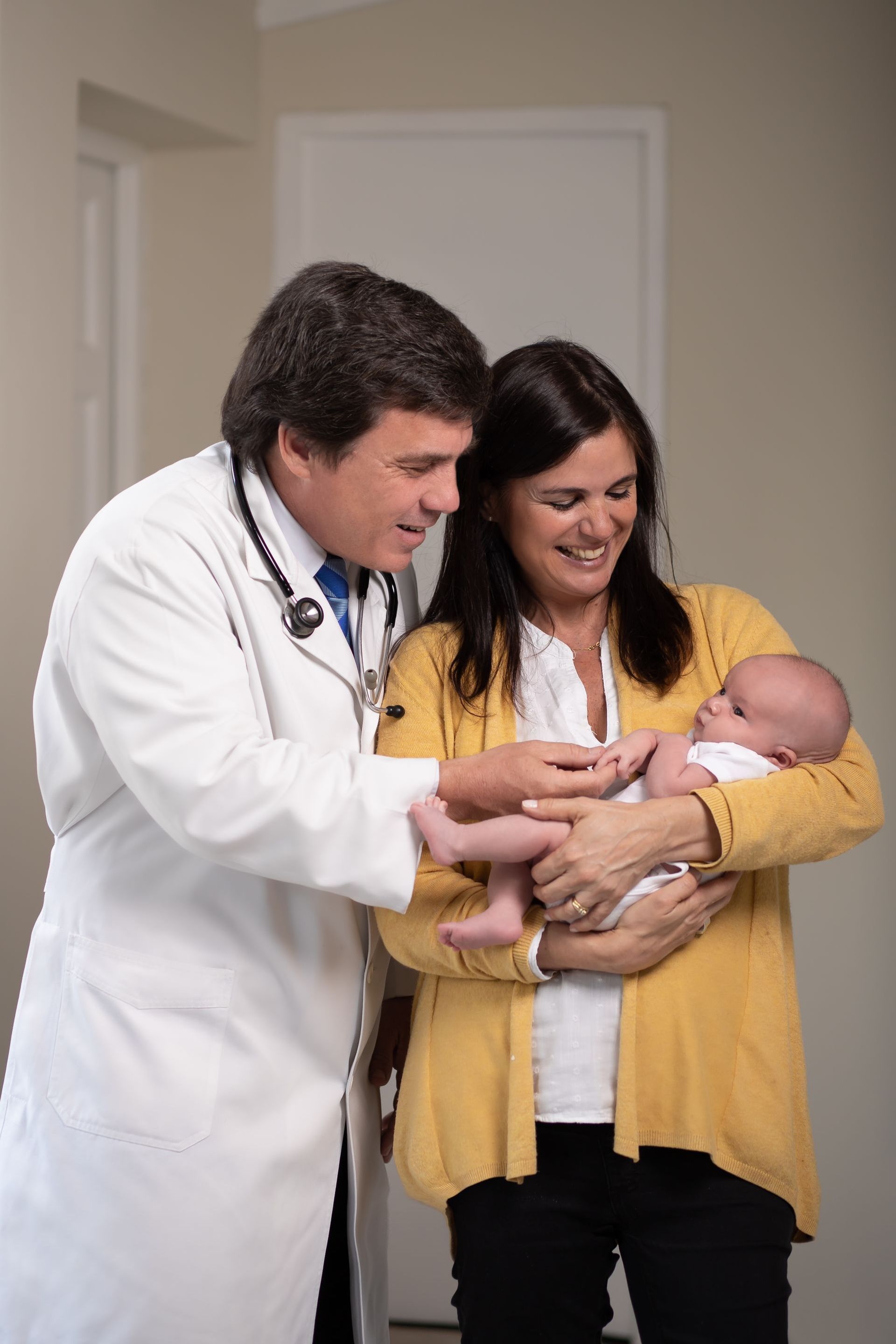Un médico examina a un bebé en brazos de uno de sus padres sonrientes en un pasillo.