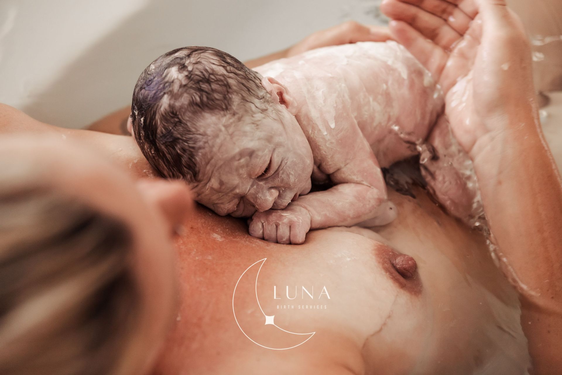 Un recién nacido es sostenido contra el pecho de uno de sus padres durante el baño, con agua tibia y espuma de jabón.