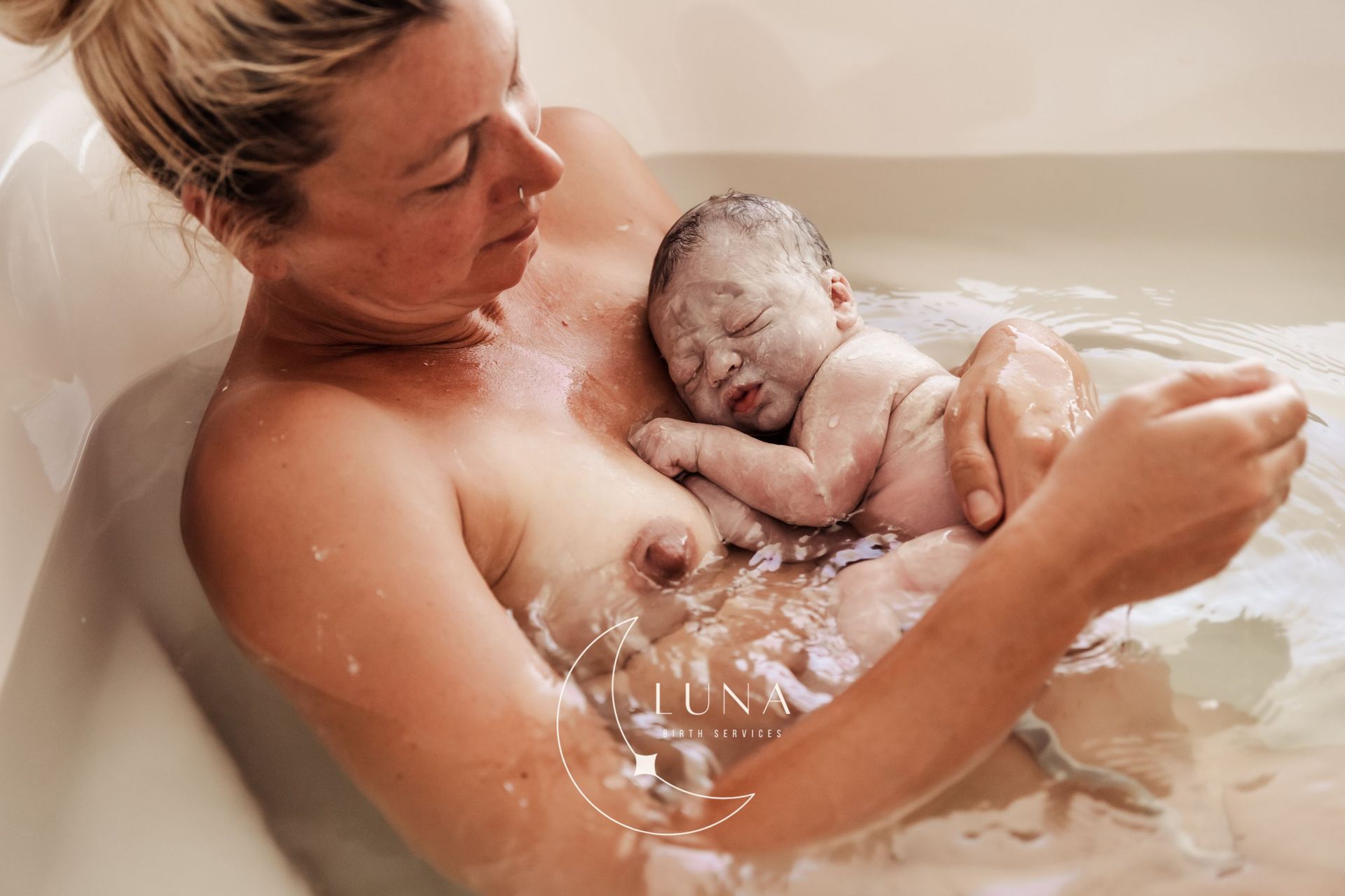 Un adulto bañando a un recién nacido dormido en una bañera con agua tibia, sosteniendo al bebé suavemente en el agua.