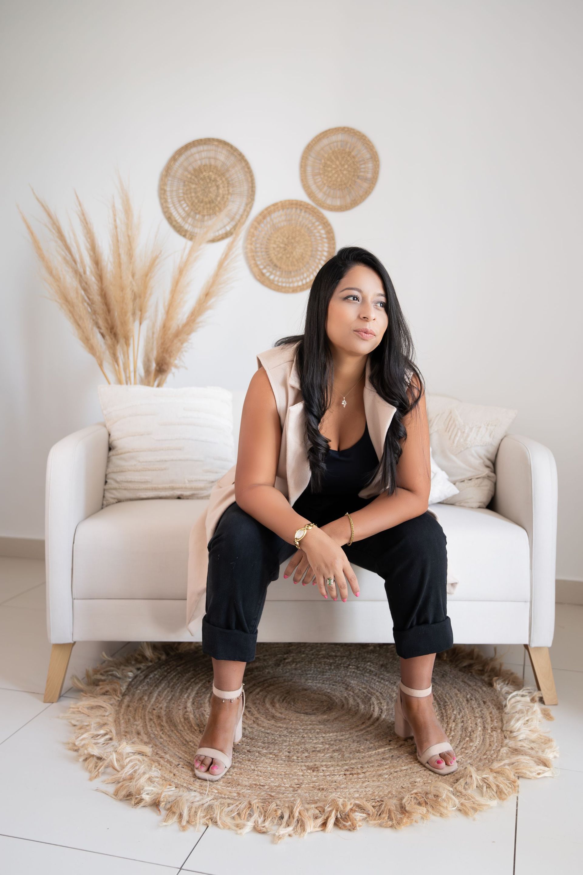 Mujer sentada en un sofá color crema en una habitación luminosa de estilo bohemio con decoración de pared tejida y hierba de la Pampa.