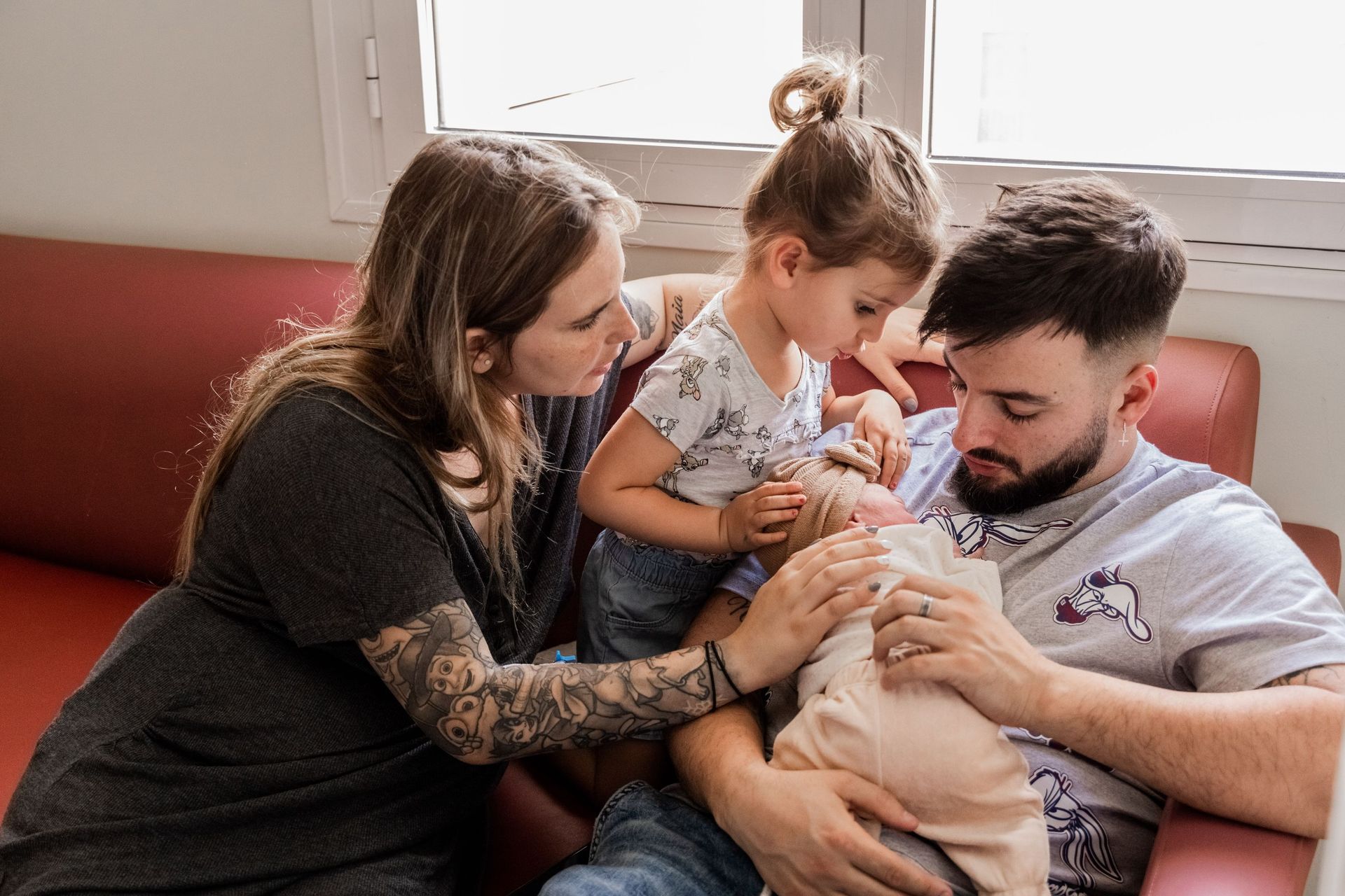 Una familia sentada en un sofá, los padres sosteniendo con ternura a un bebé y a un niño pequeño en una luminosa sala de estar.