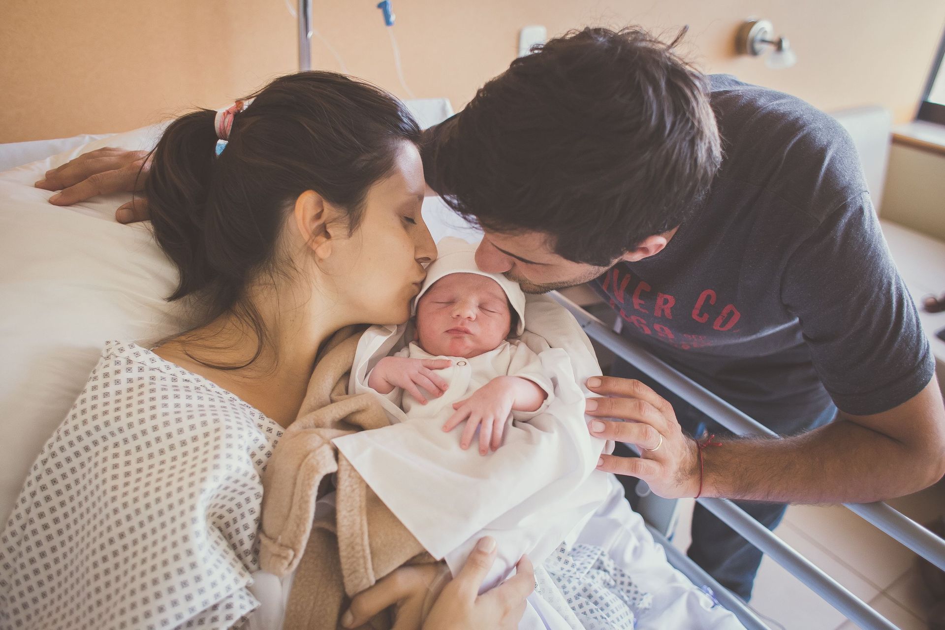 Los padres besan a su recién nacido en la cama del hospital, envuelto en una manta.