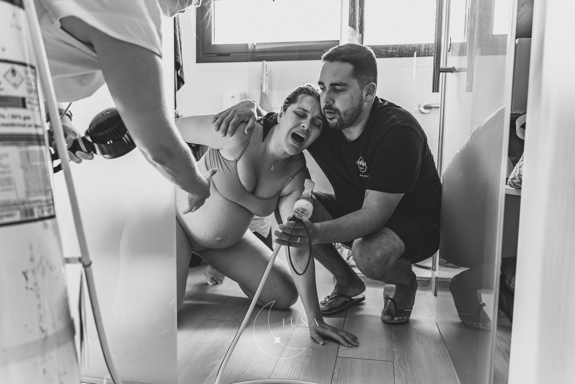 En una escena de estudio en blanco y negro, una persona se agacha junto a otra sentada, sosteniéndola durante una pose.