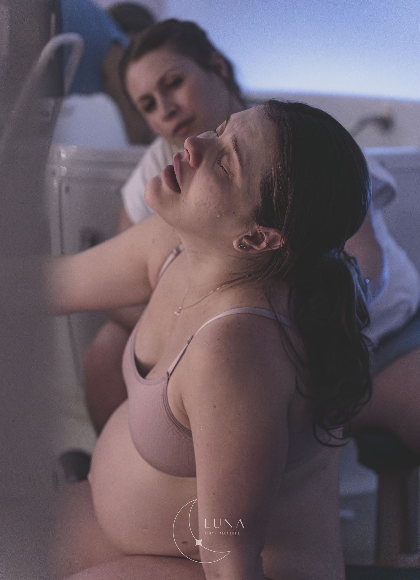Dos mujeres sentadas en el interior, una de ellas recostada con los ojos cerrados, vestidas con camisetas de tirantes rosas.