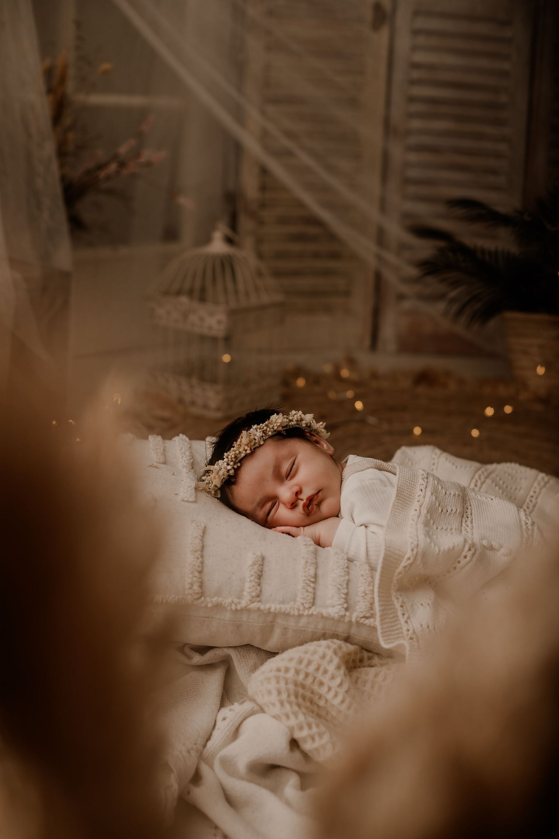 Bebé durmiendo con un conjunto de punto color crema, descansando sobre una almohada blanca en una acogedora habitación infantil con iluminación tenue y luces centelleantes.