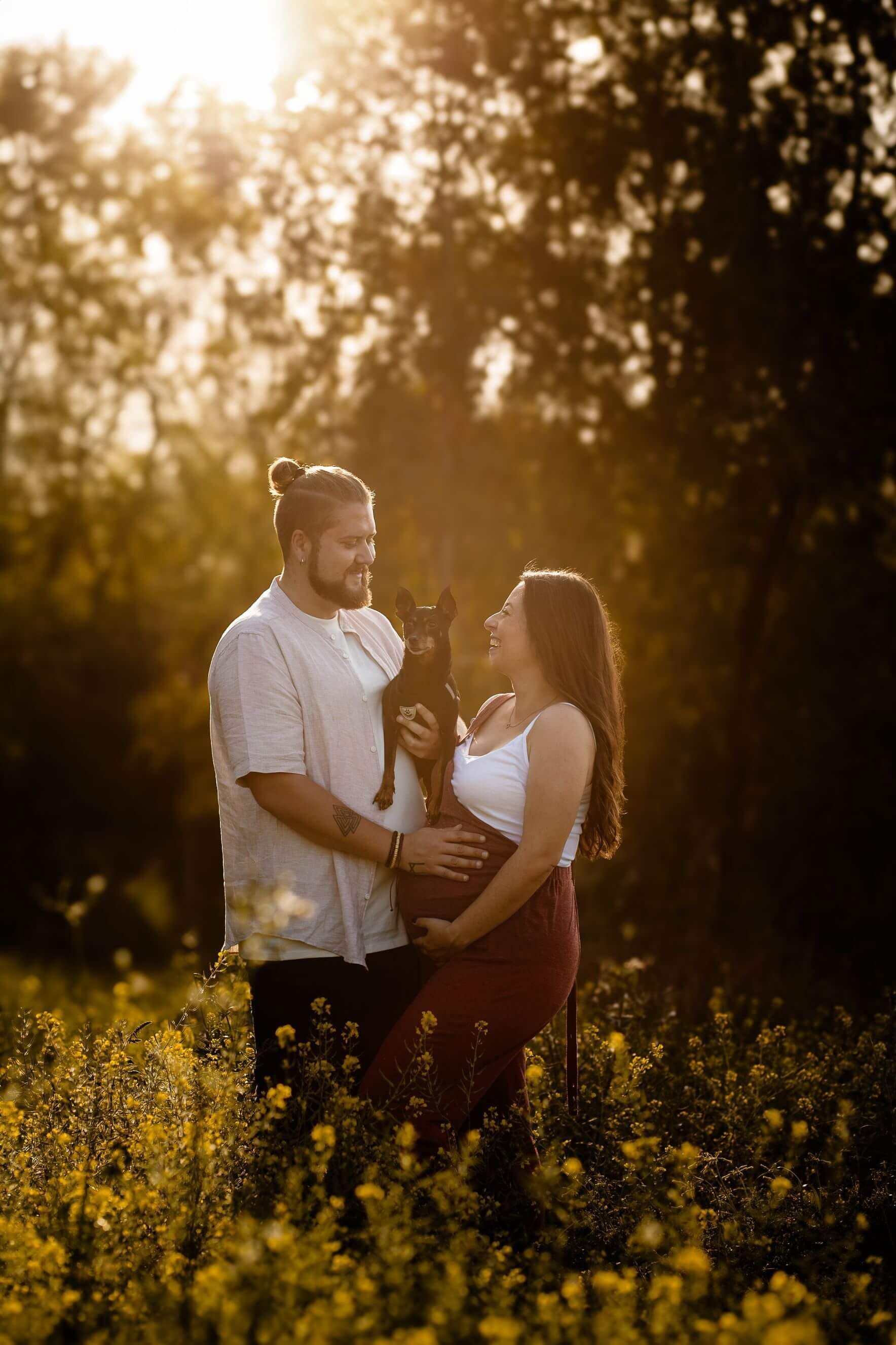 Una pareja se encuentra en un campo iluminado por el sol, abrazándose y mirándose el uno al otro al atardecer.