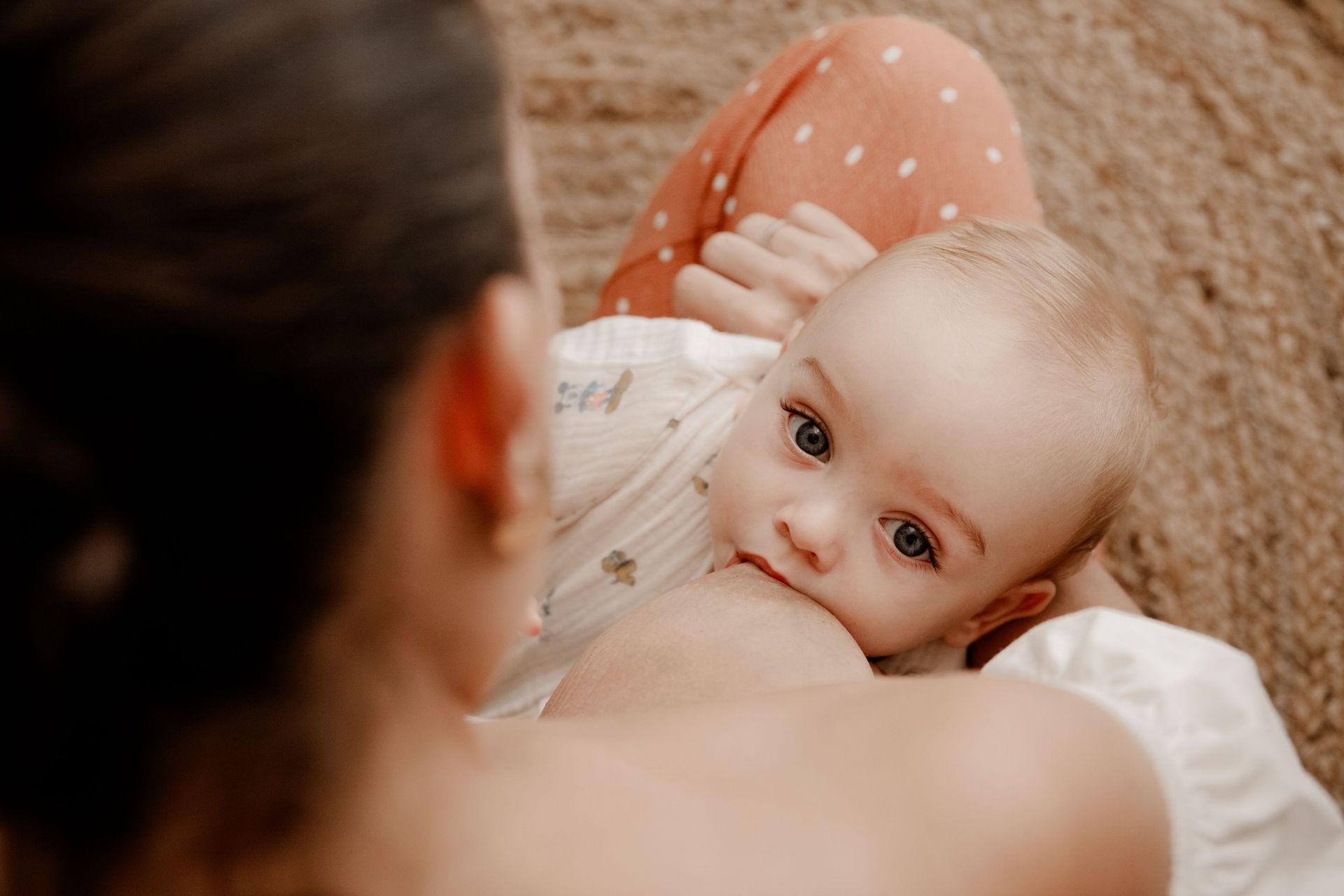 Una madre primeriza amamanta a su recién nacido en la cama, envuelto en una manta blanca.