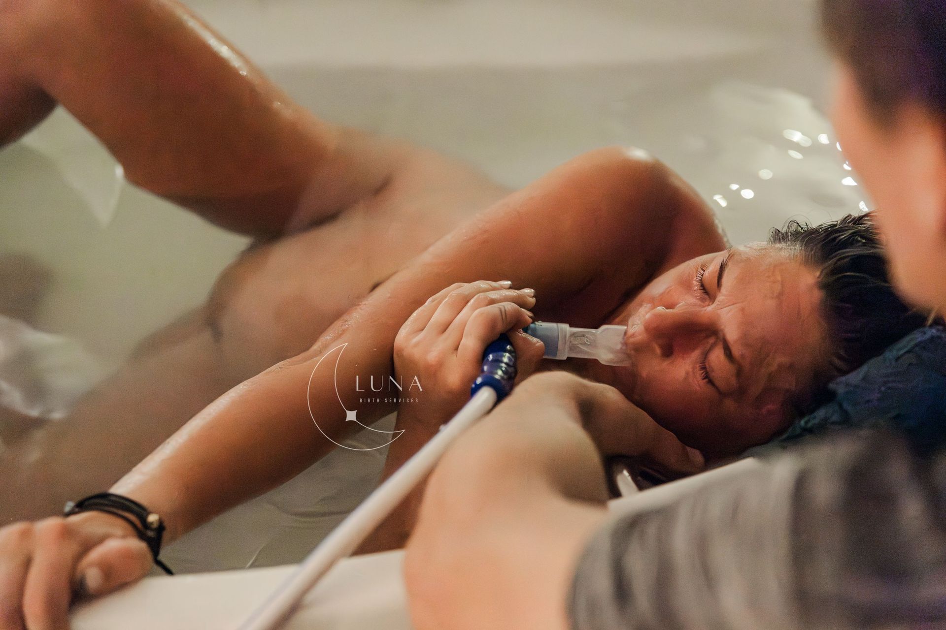 Un recién nacido es sostenido en una piscina de parto mientras un cuidador asiste en el alumbramiento.