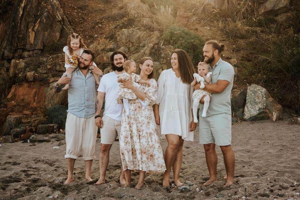 Grupo de personas posando al aire libre al atardecer con perros, vistiendo ropa de colores claros en un paisaje rocoso.