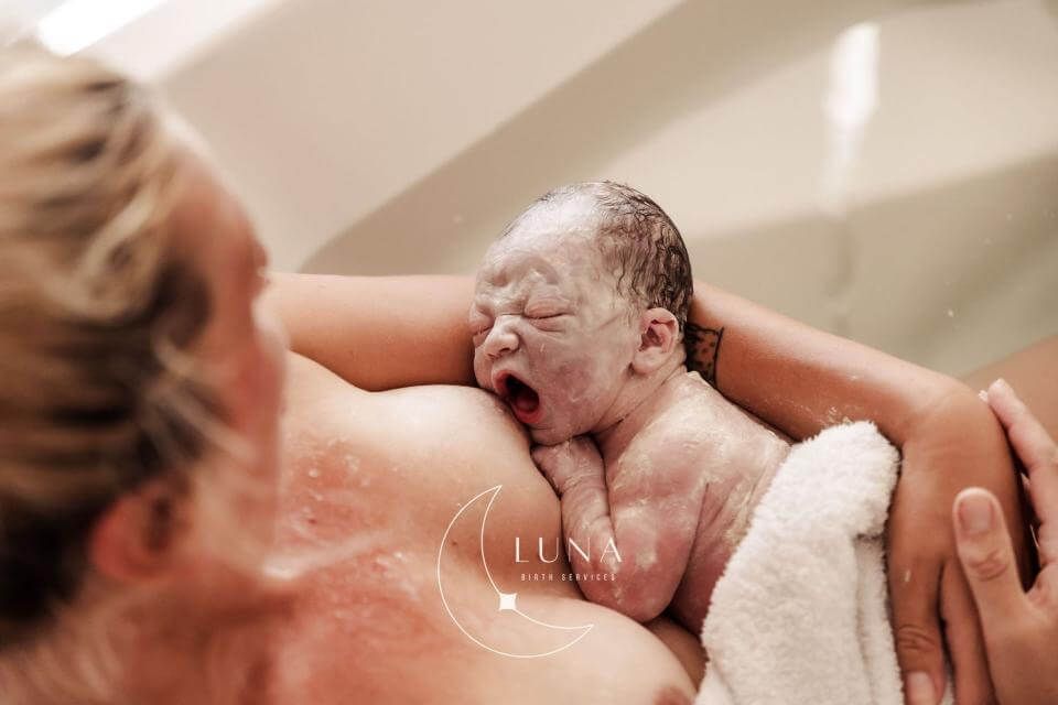 Un recién nacido es bañado suavemente, cubierto de espuma y sostenido en brazos por un adulto.
