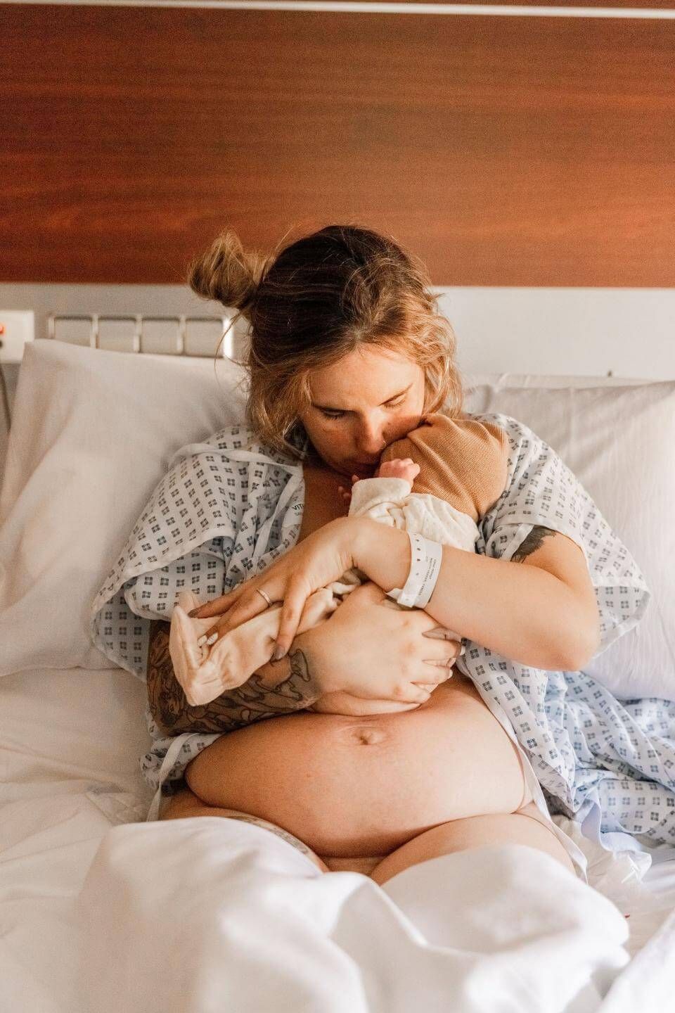 Madre besando a su bebé recién nacido mientras está acostada en la cama.