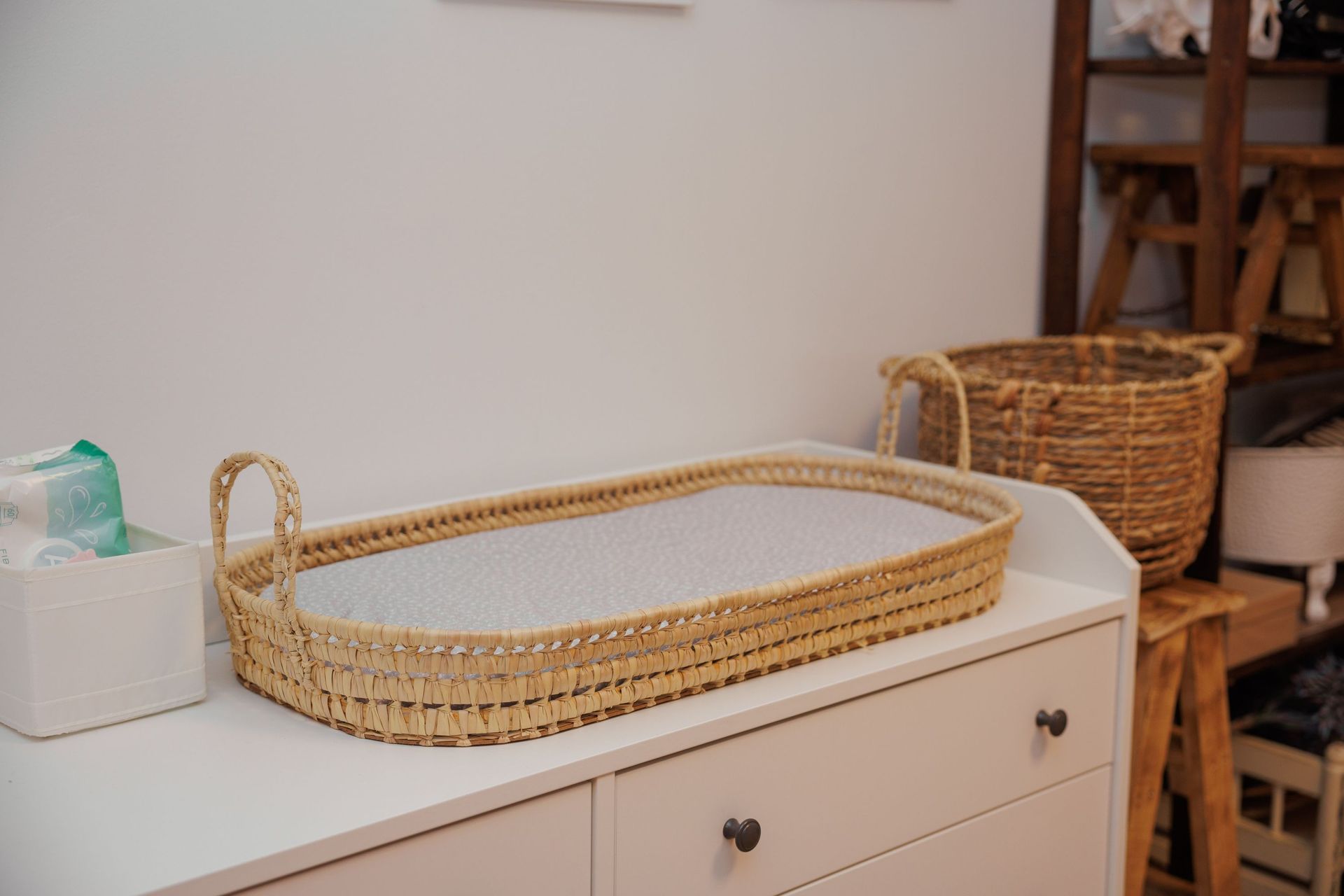 Bandeja de mimbre tejida sobre una cómoda blanca en una habitación acogedora con cestas y estantes cerca.