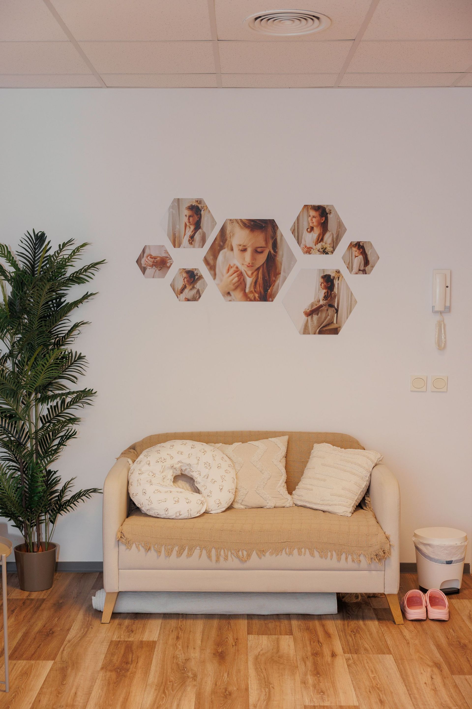 Acogedora habitación infantil con un sofá de dos plazas color beige, un collage de fotos en la pared, una planta en maceta y suelo de madera noble.