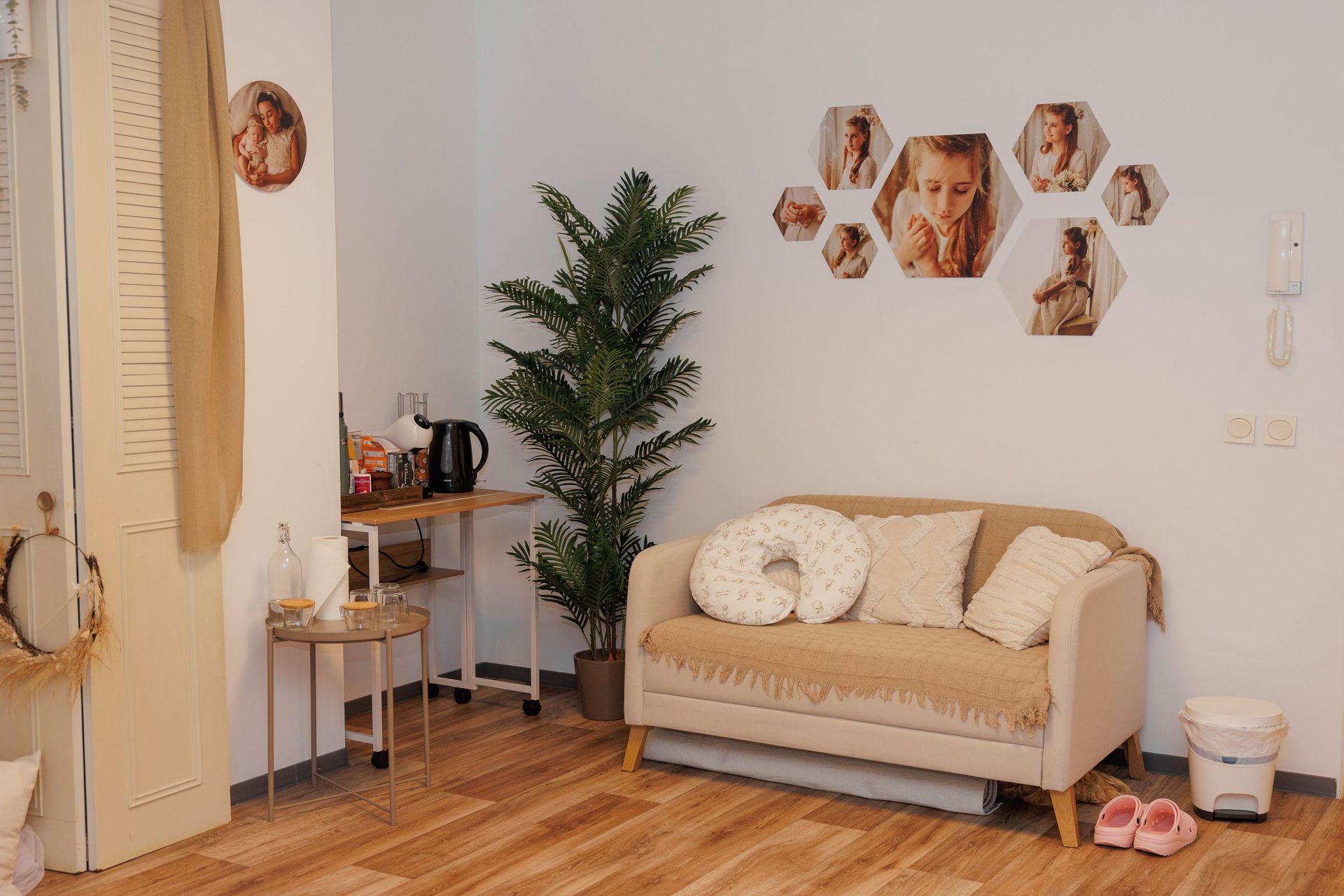 Acogedora sala de estar de color beige con sofá, retratos en la pared, planta en maceta y cálido suelo de madera.
