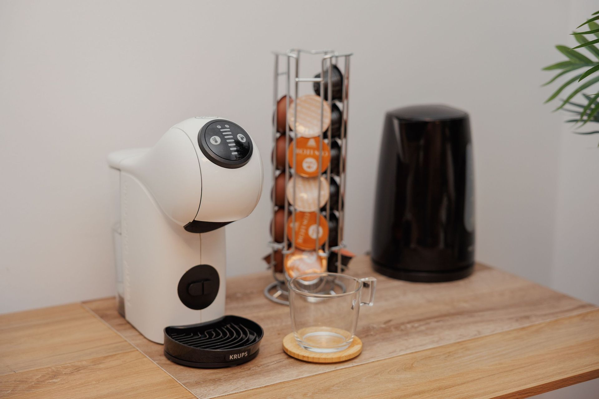 Cafetera y cápsulas sobre una encimera de madera junto a un recipiente negro.