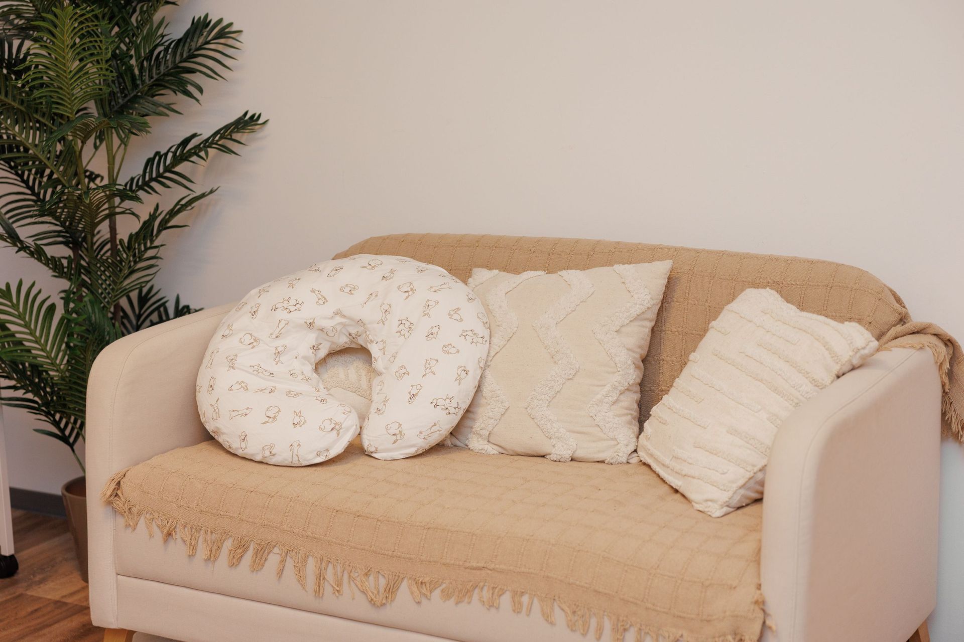 Sofá beige con cojines color crema y un cojín cervical en forma de U junto a una planta en maceta.