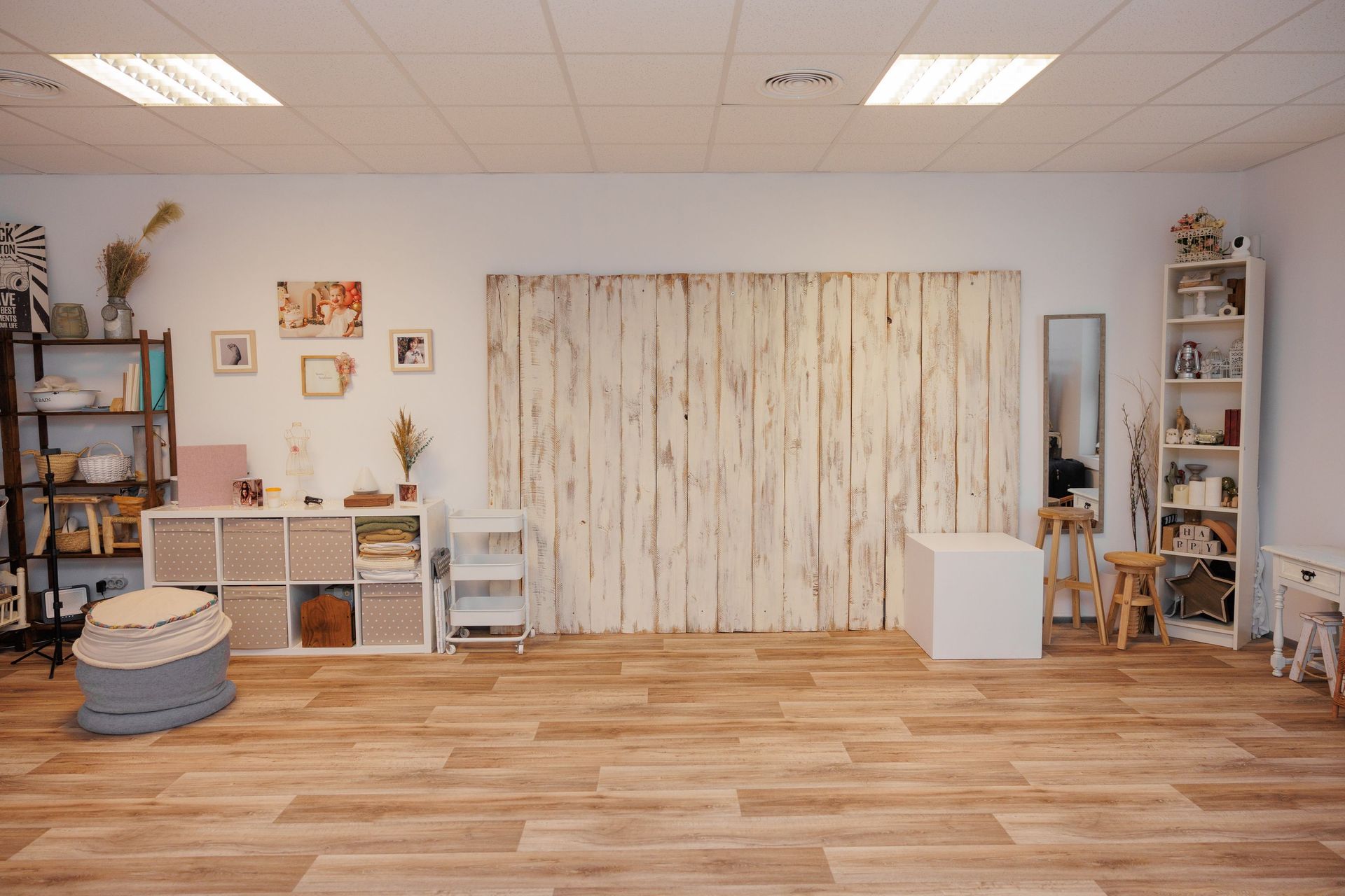 Estudio luminoso con suelos de madera, cortinas, estanterías, cestas y una zona de juegos central.