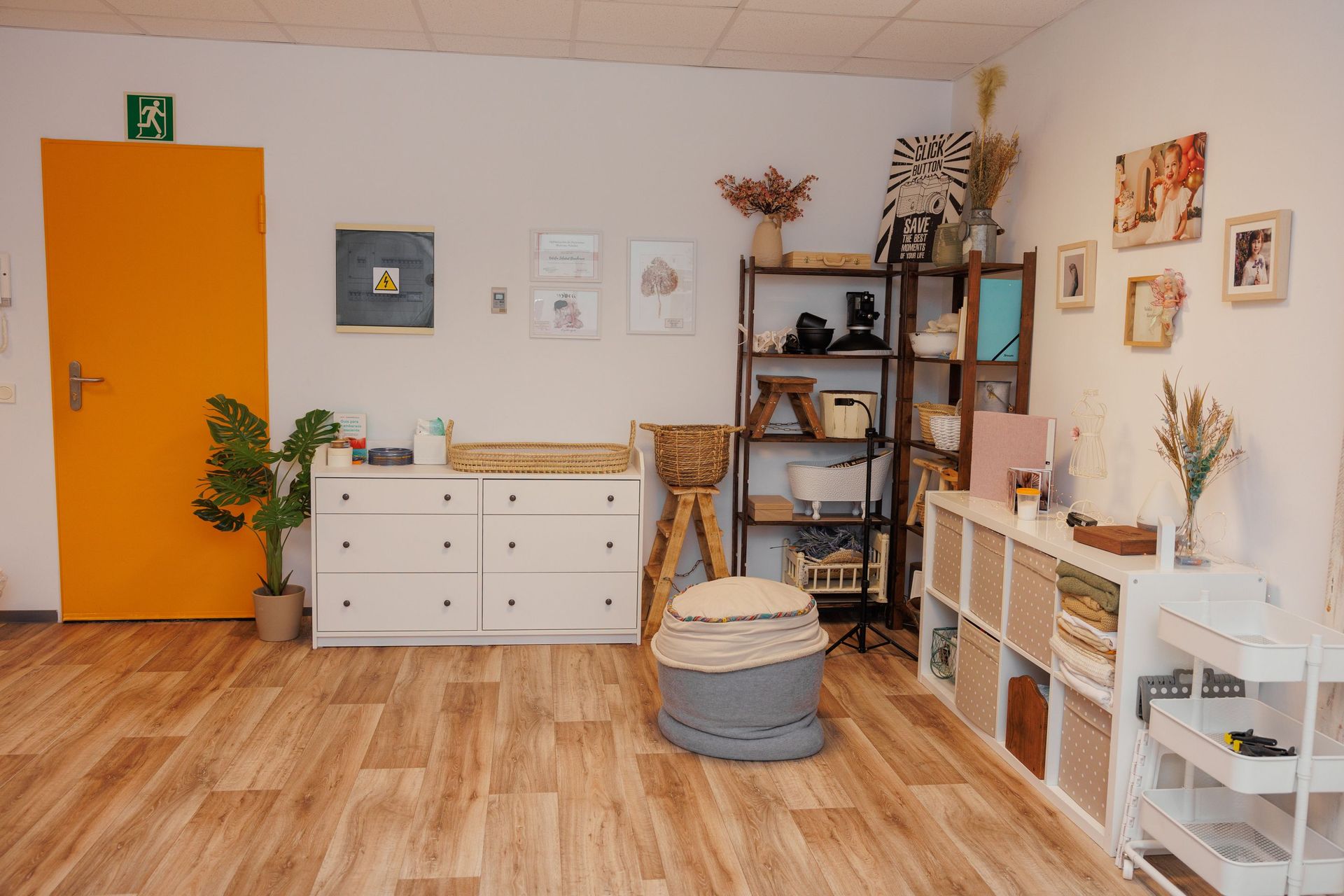 Habitación acogedora con puerta naranja, cómoda blanca, estantes, plantas y decoración de mimbre sobre suelo de madera.