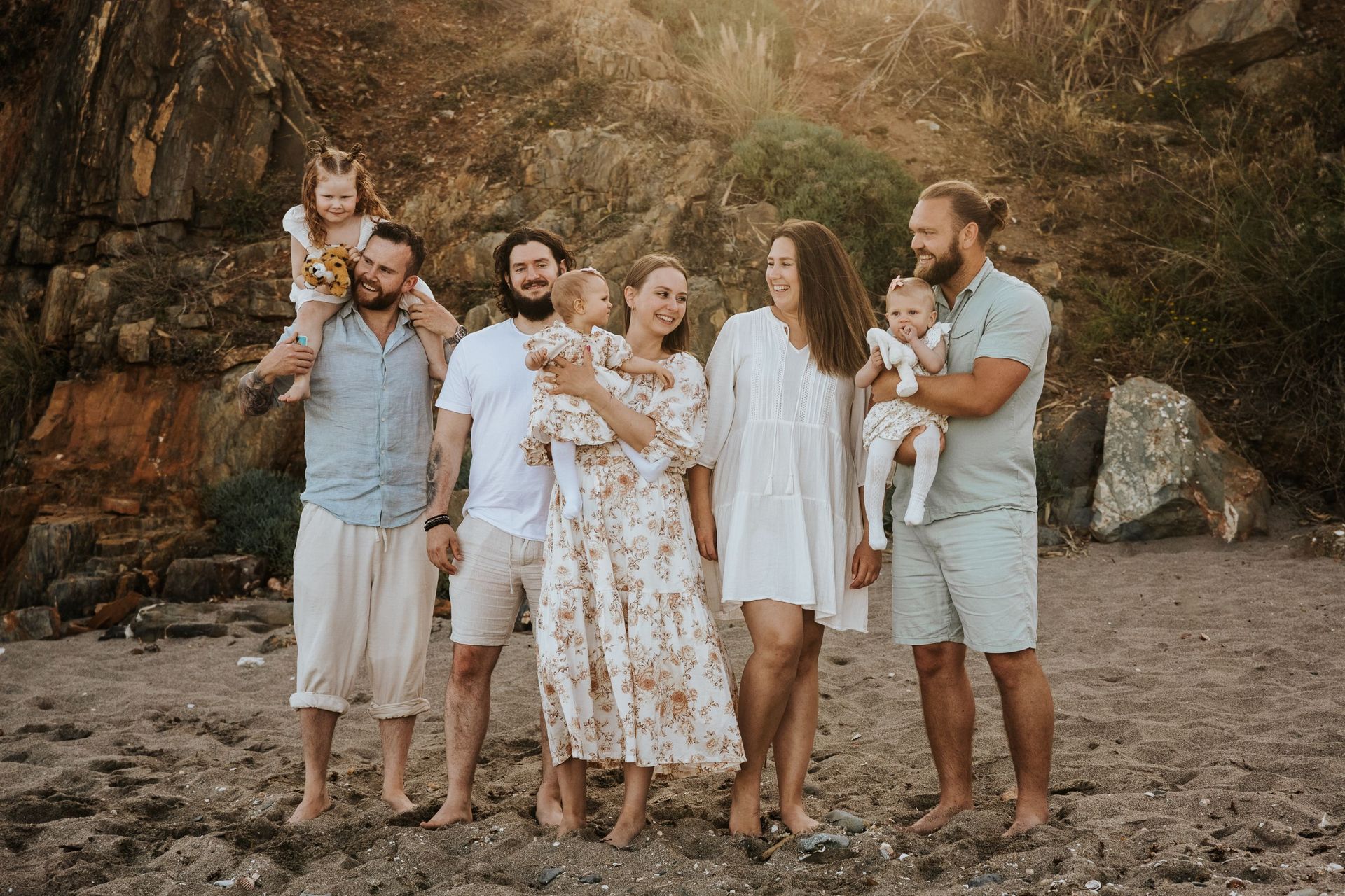 Grupo de personas posando al aire libre al atardecer con perros, vistiendo ropa de colores claros en un paisaje rocoso.