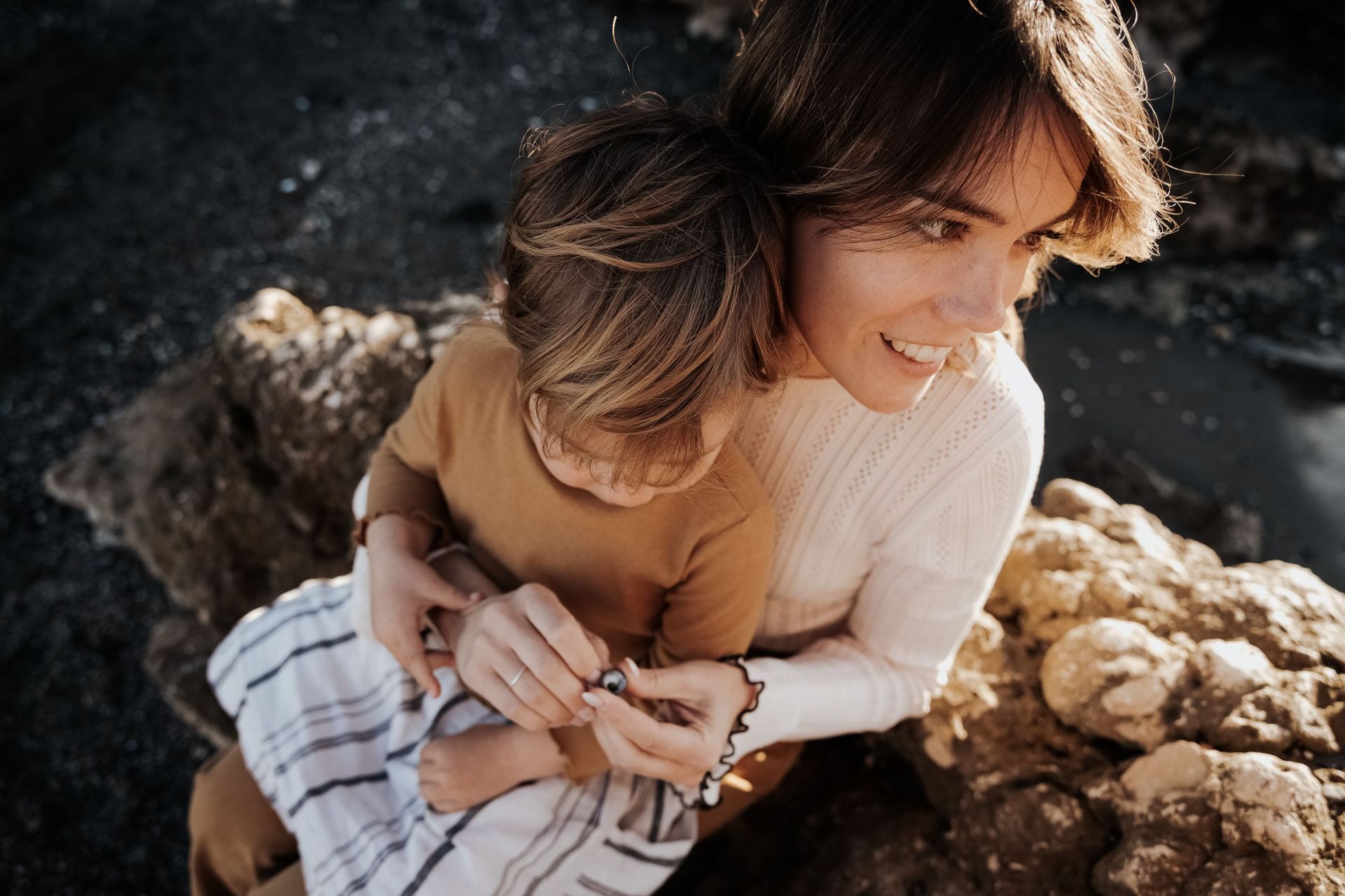 Dos personas se abrazan al aire libre sobre rocas iluminadas por el sol, sonriendo cálidamente.
