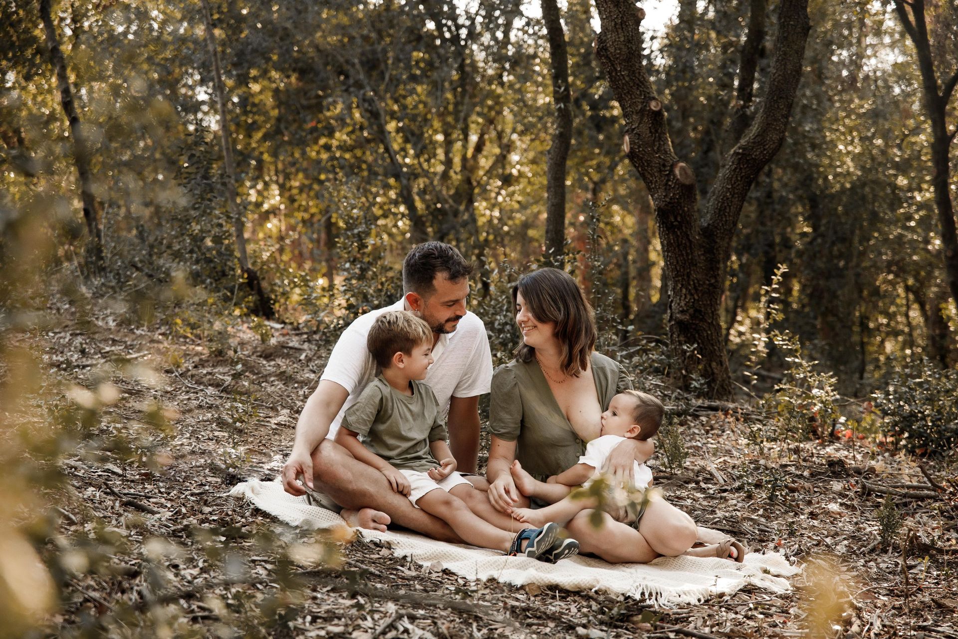Una familia sentada sobre una manta en un bosque soleado, compartiendo un momento de tranquilidad juntos.